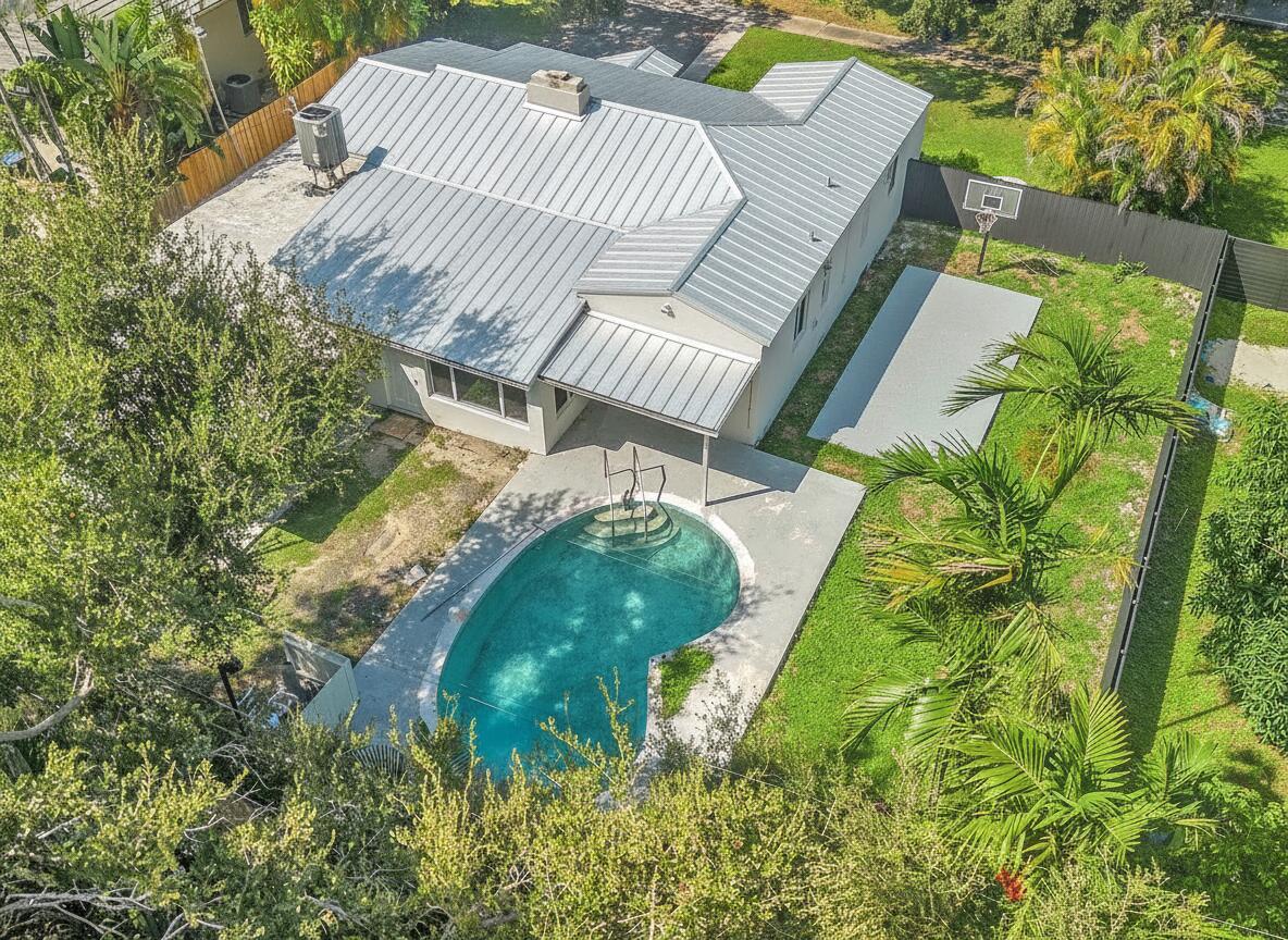 Aerial view of a home with a curved pool, paved patio, and fenced backyard with a basketball hoop.