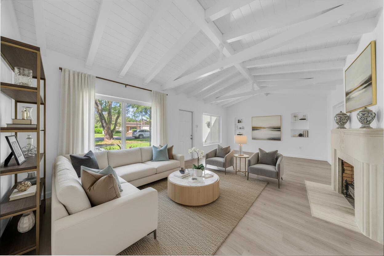 Staged living room with vaulted beam ceiling, white sectional, and fireplace.