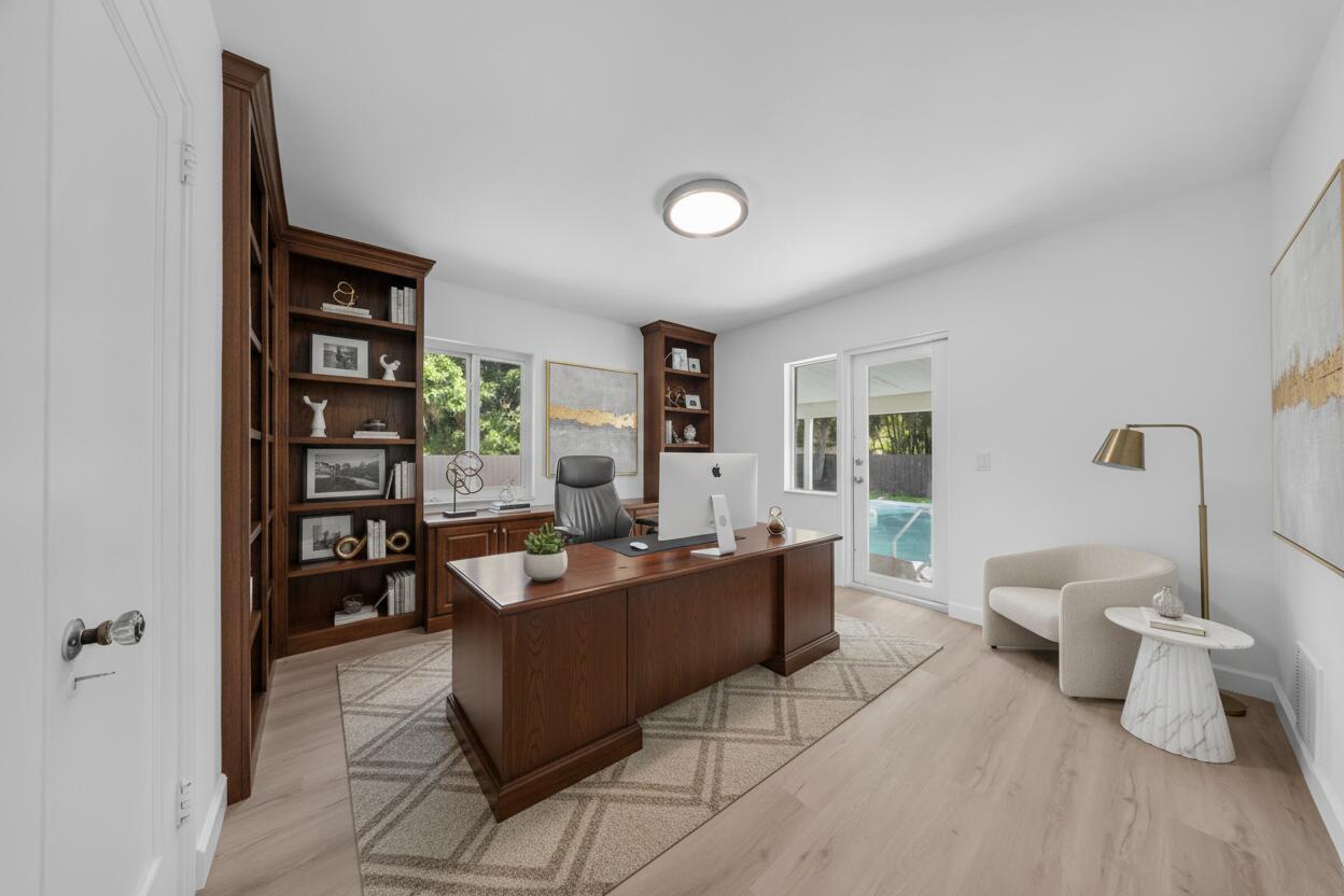 Home office with a large wood desk, built-in bookshelves, and glass doors overlooking the pool.