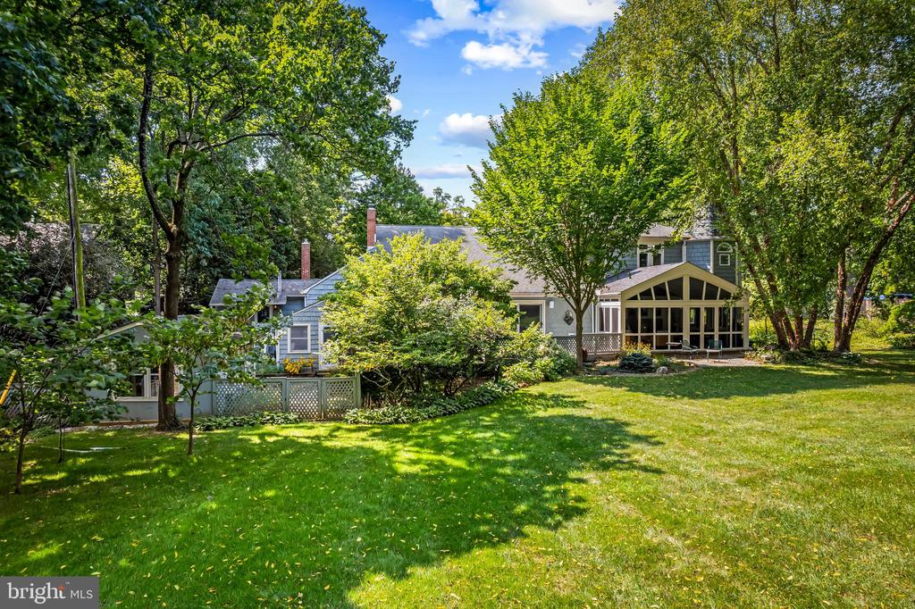 House rear with glass-enclosed sunroom, mature trees, and a broad lawn.