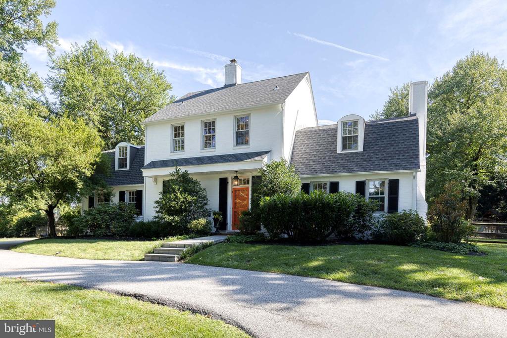 White two-story house with an orange front door, black shutters, and a landscaped lawn.