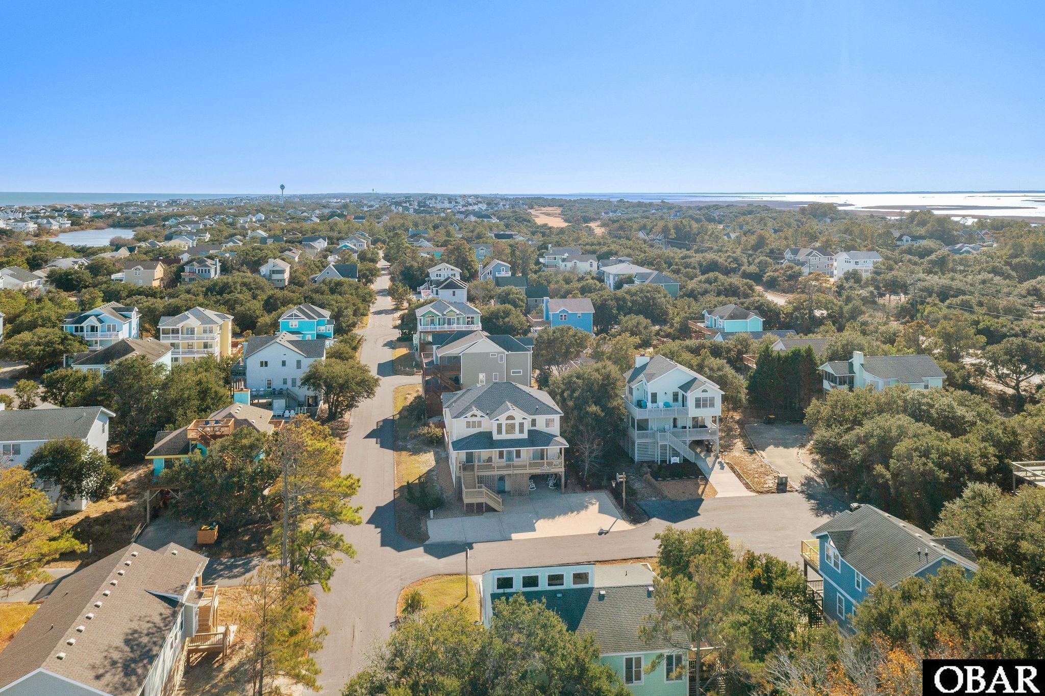 Aerial view of coastal homes and a winding street, with water on the horizon.