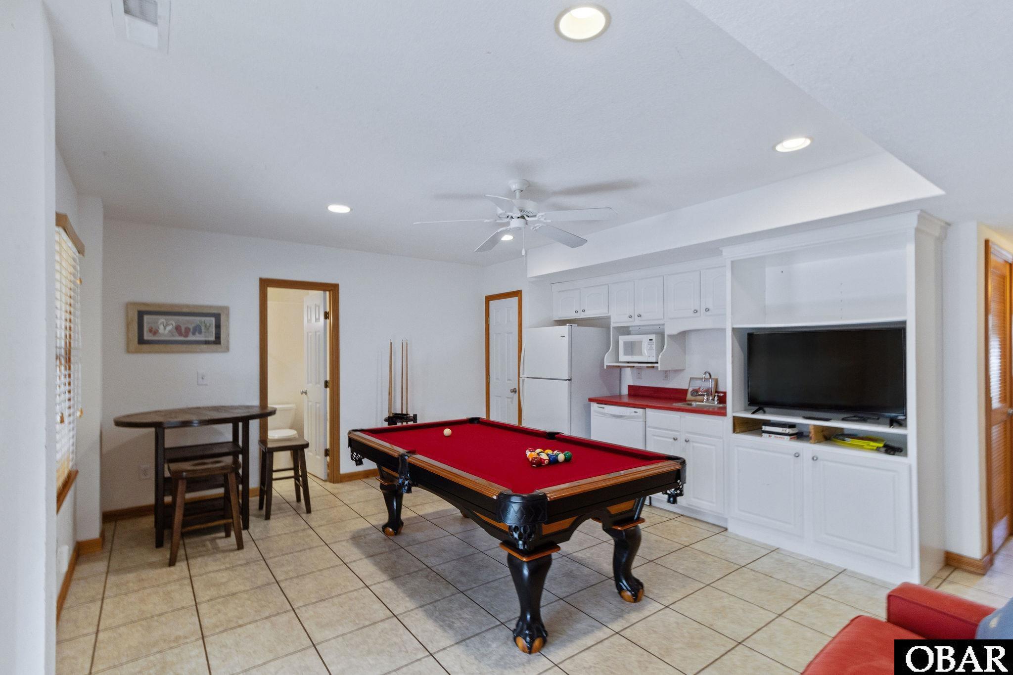 Game room with a red-felt pool table, white kitchenette, built-in television, and tile flooring.