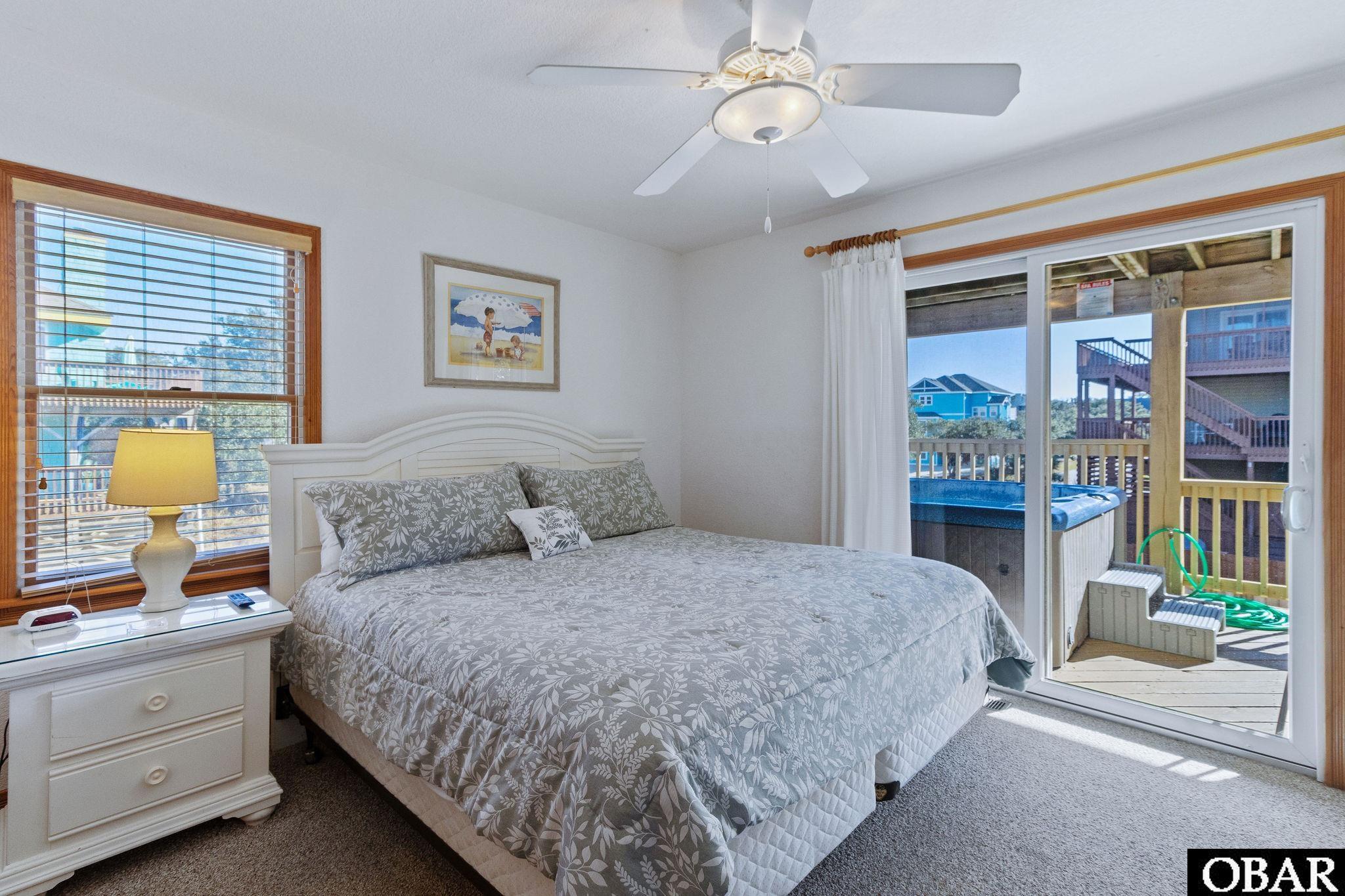 Bedroom with a gray floral bed and sliding doors opening to a deck with a hot tub.