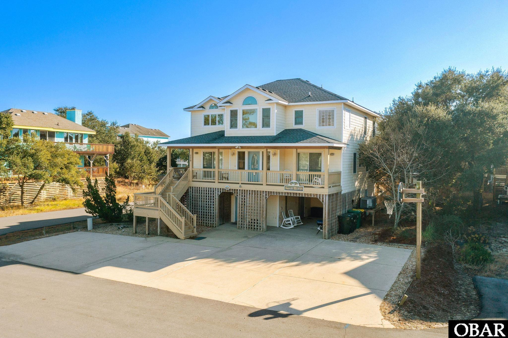 Two-story coastal home with a covered porch, elevated foundation, and broad concrete driveway.