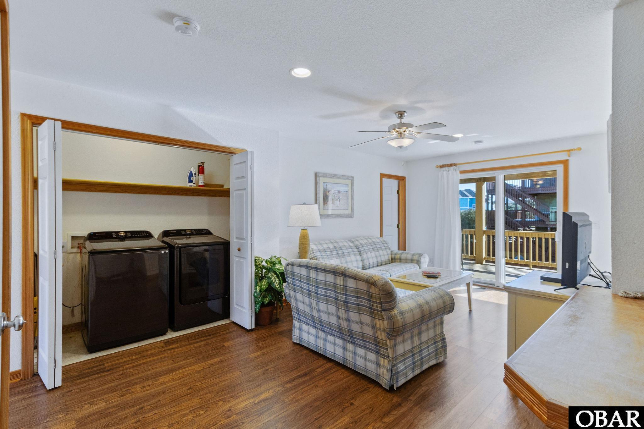 Living room with plaid sofas, sliding doors to a deck, and washer and dryer behind folding doors.