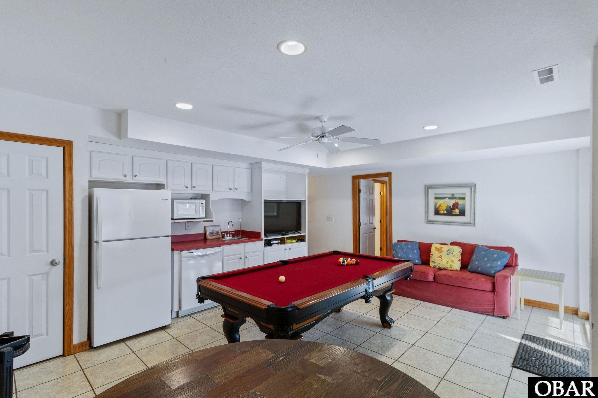 Game room with a red-felt pool table, kitchenette, and pink sofa.