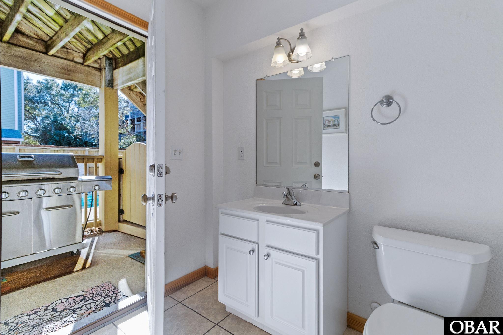 Bathroom with a white vanity and toilet opening onto a covered deck with a stainless-steel grill.