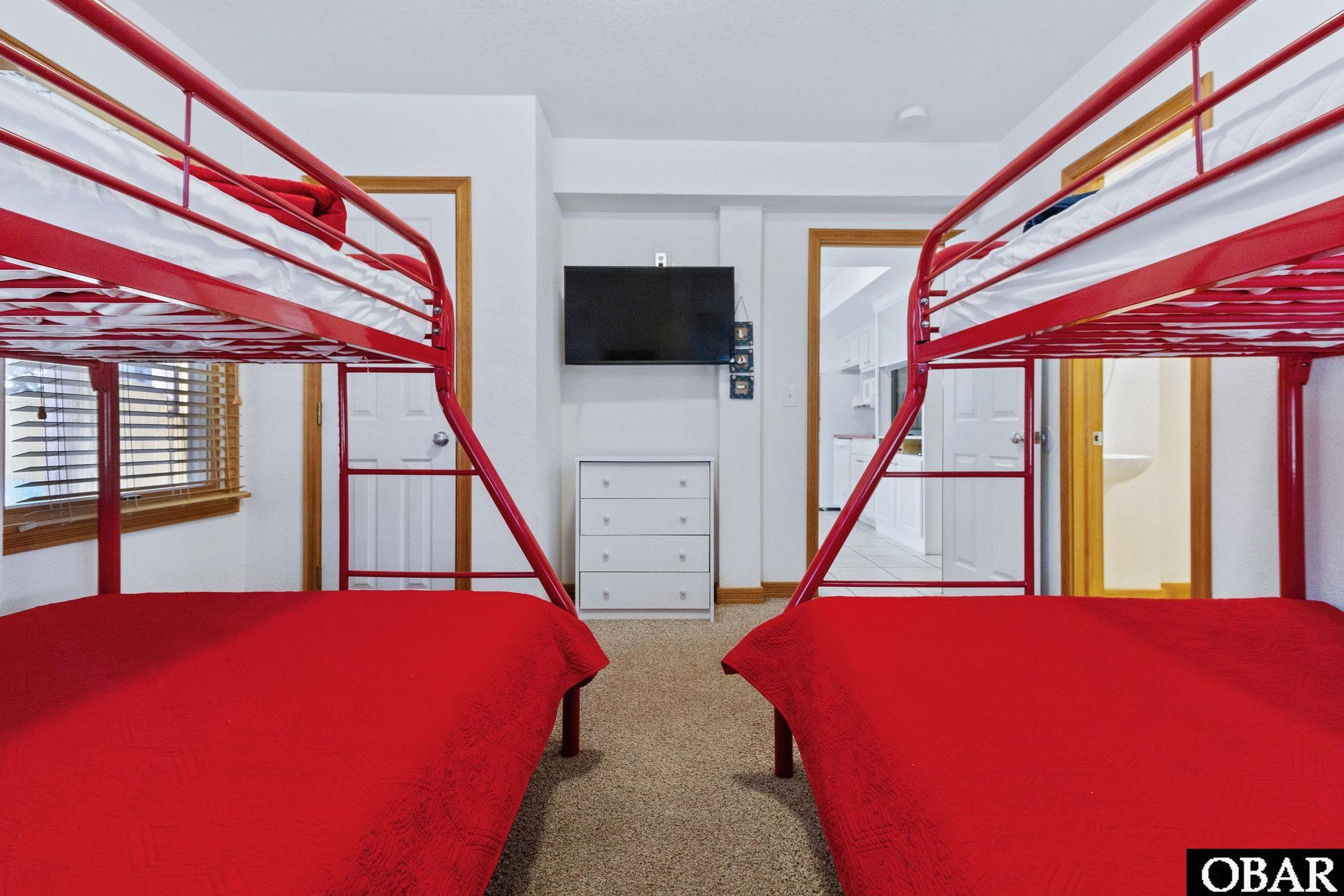 Bedroom with two red bunk beds, a white dresser, and a wall-mounted television.