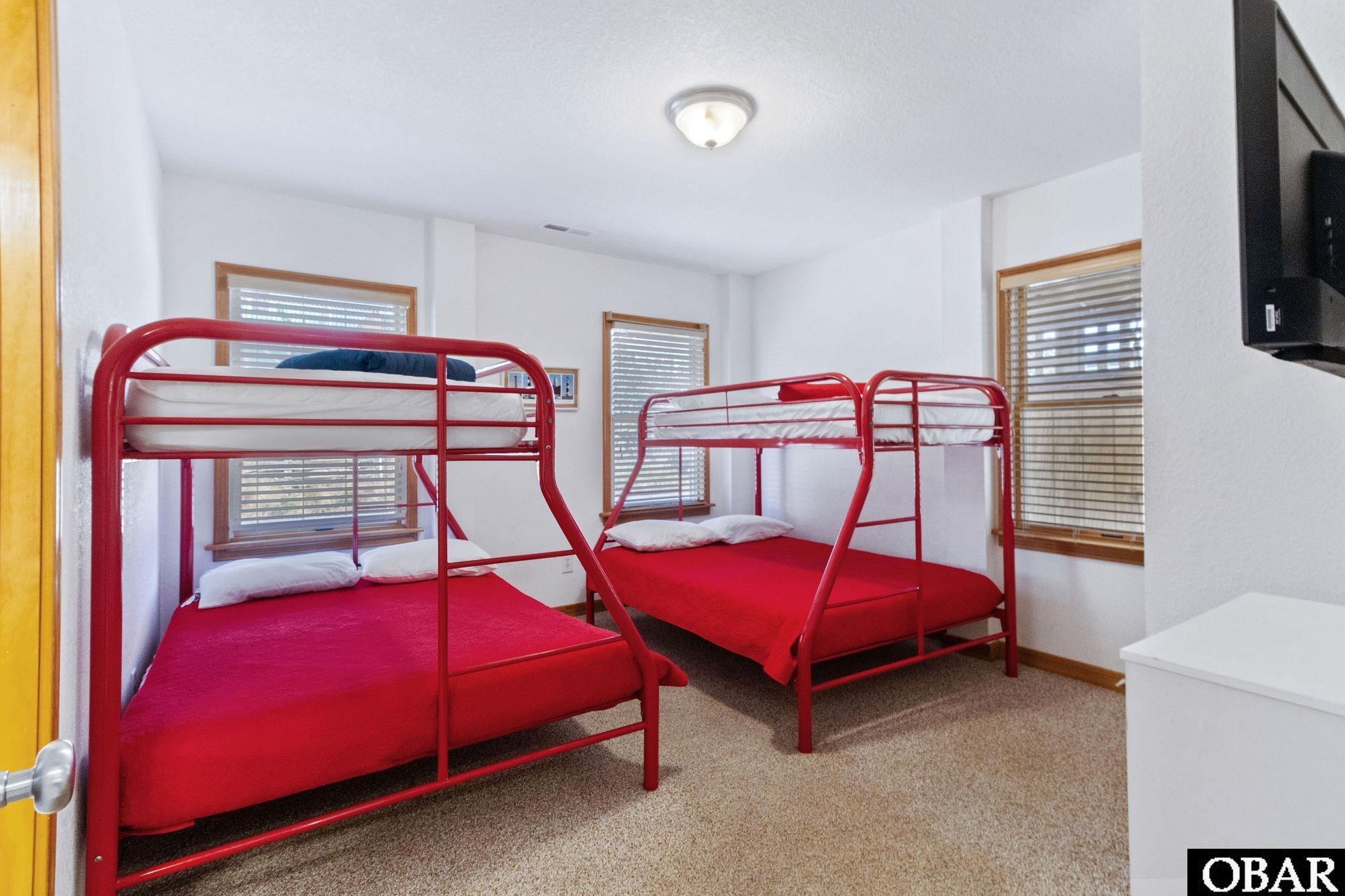 Bedroom with two red metal bunk beds and wood-trimmed windows.