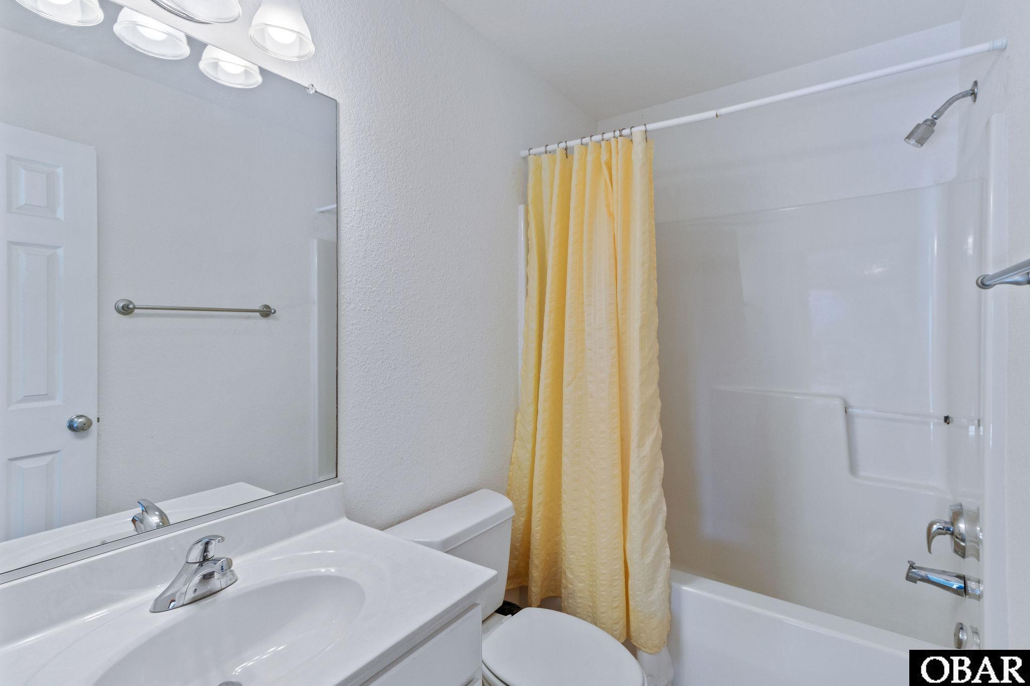 Bathroom with a white vanity, tub and shower, and yellow curtain.