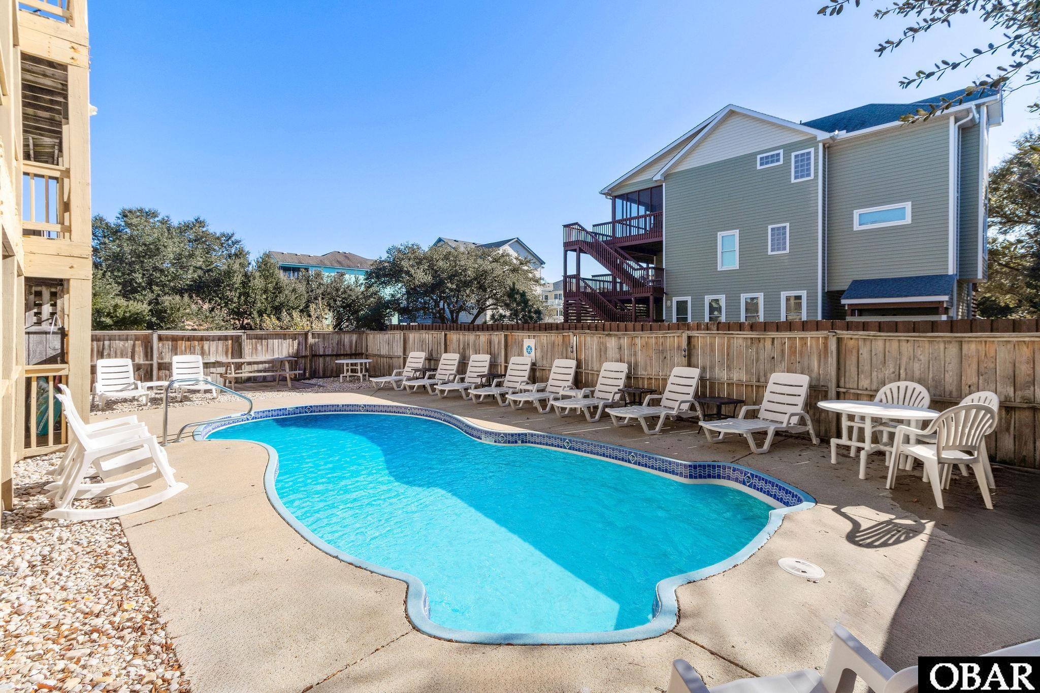 Outdoor swimming pool with a curved shape, surrounding lounge chairs, and a fenced deck.