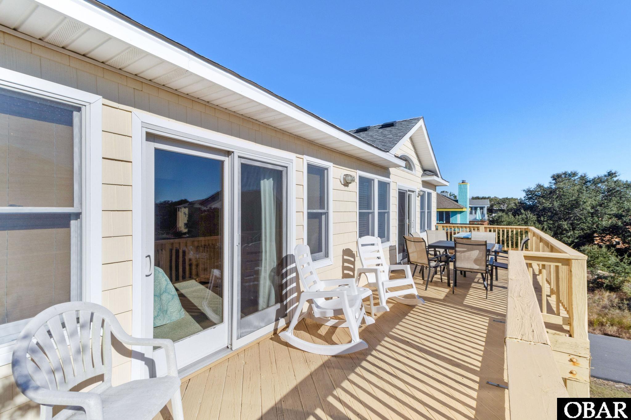 Furnished wooden deck with white rocking chairs and patio dining furniture beside the house.