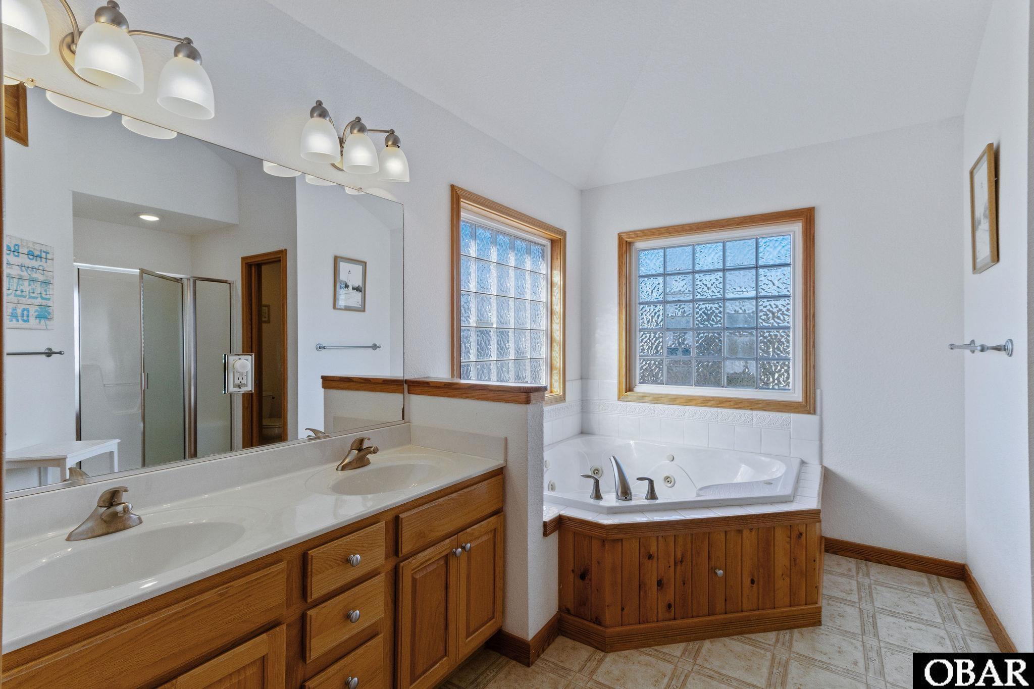 Bathroom with a wood double-sink vanity, corner jetted tub, and textured-glass windows.