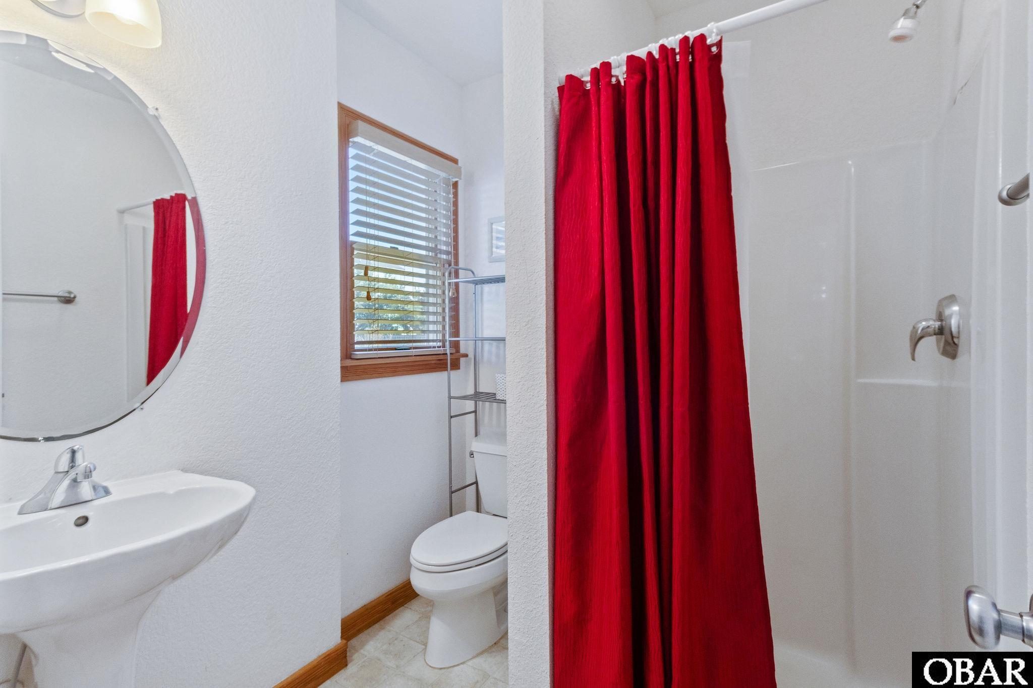 Bathroom with a bright red shower curtain, white sink, and toilet beside a window.