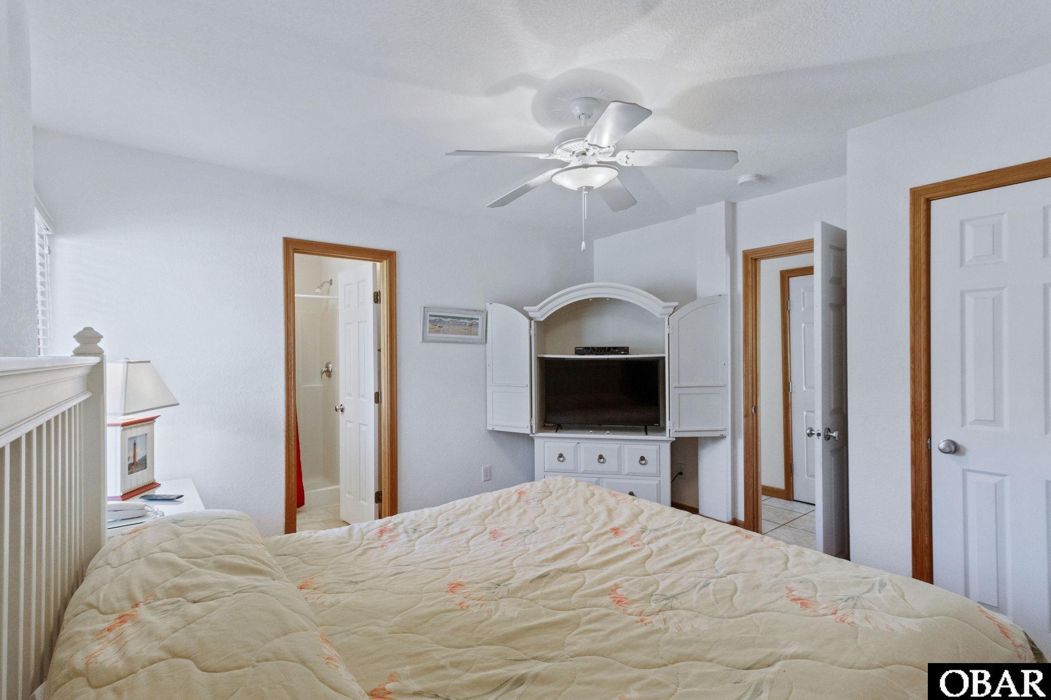 Bedroom with a large bed and a white built-in television cabinet beneath a ceiling fan.