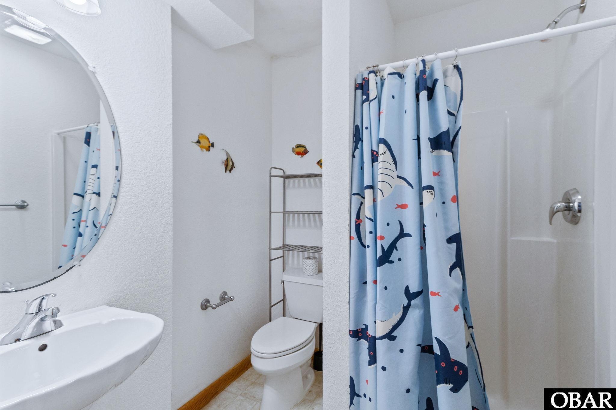 Bathroom with an oval mirror, white sink, toilet, and blue sea-creature shower curtain.