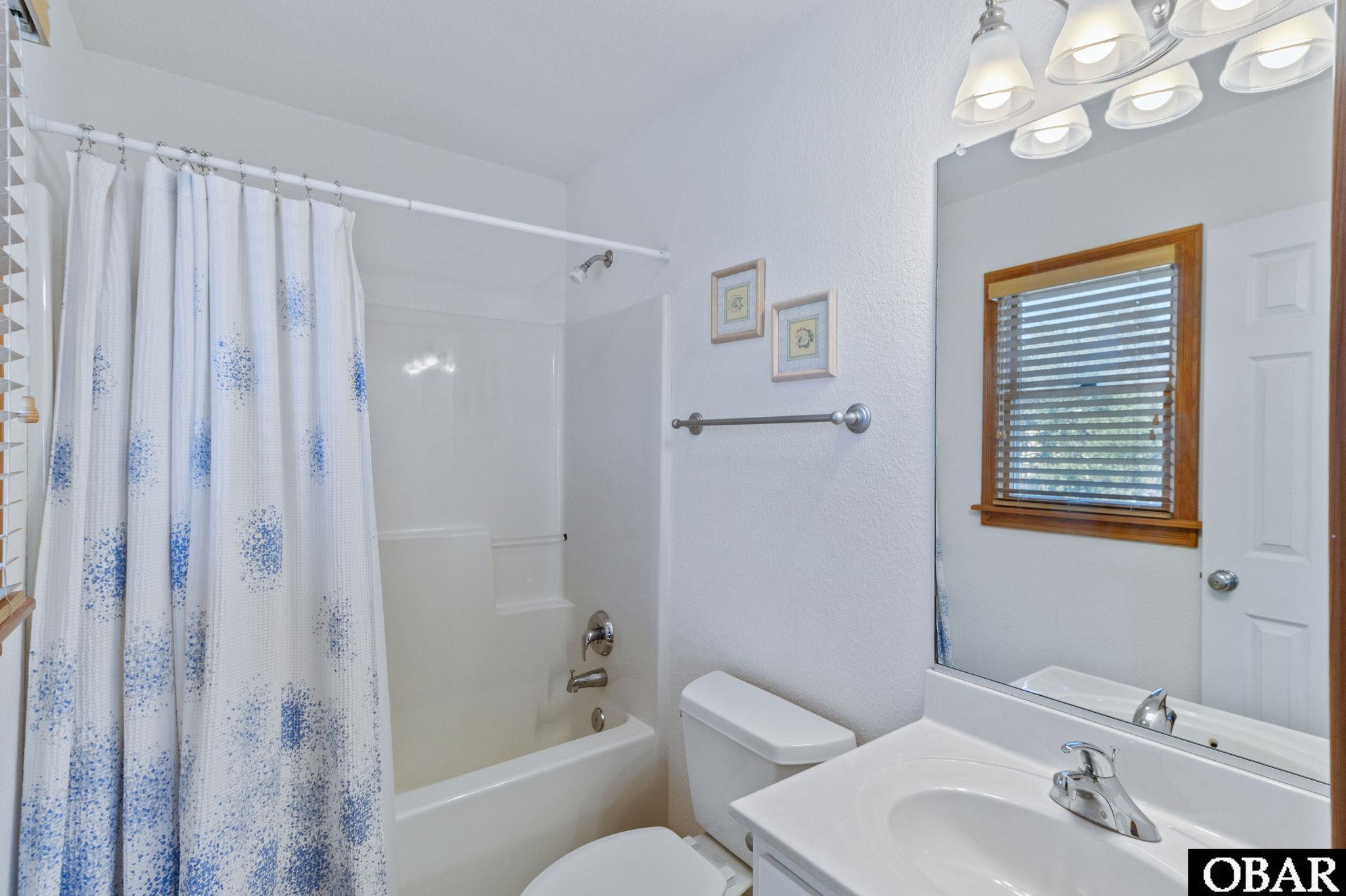 Bathroom with a blue-speckled shower curtain, white tub, toilet, and sink vanity.
