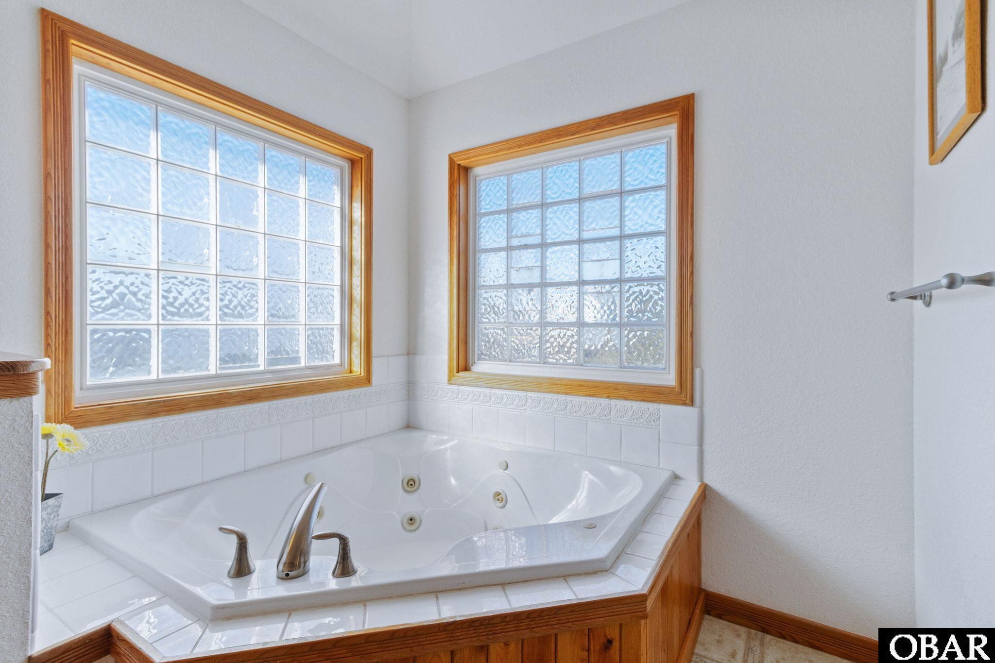 Bathroom with a built-in jetted tub beneath two large wood-trimmed windows.
