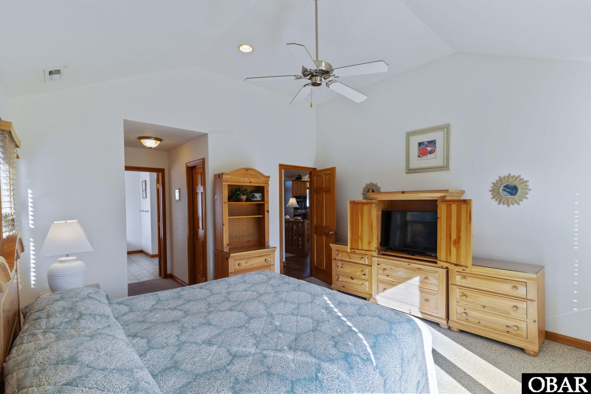 Furnished bedroom with blue patterned bedding, light wood furniture, and a ceiling fan.