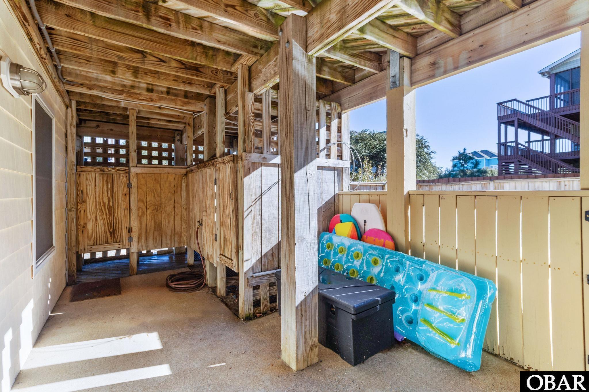 Covered outdoor shower beneath a raised house, with colorful pool floats beside the railing.