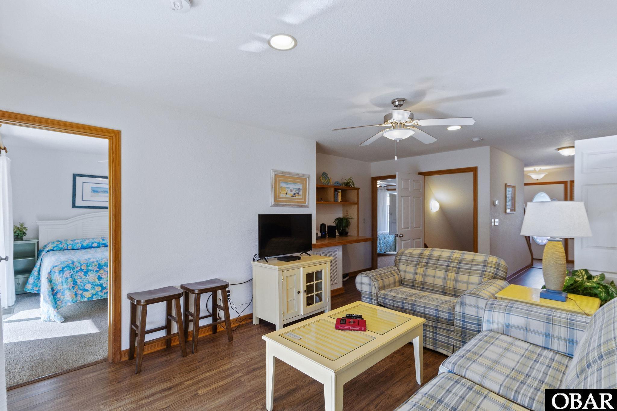 Living room with plaid sofas, pale coffee table, and an open view into a bedroom.