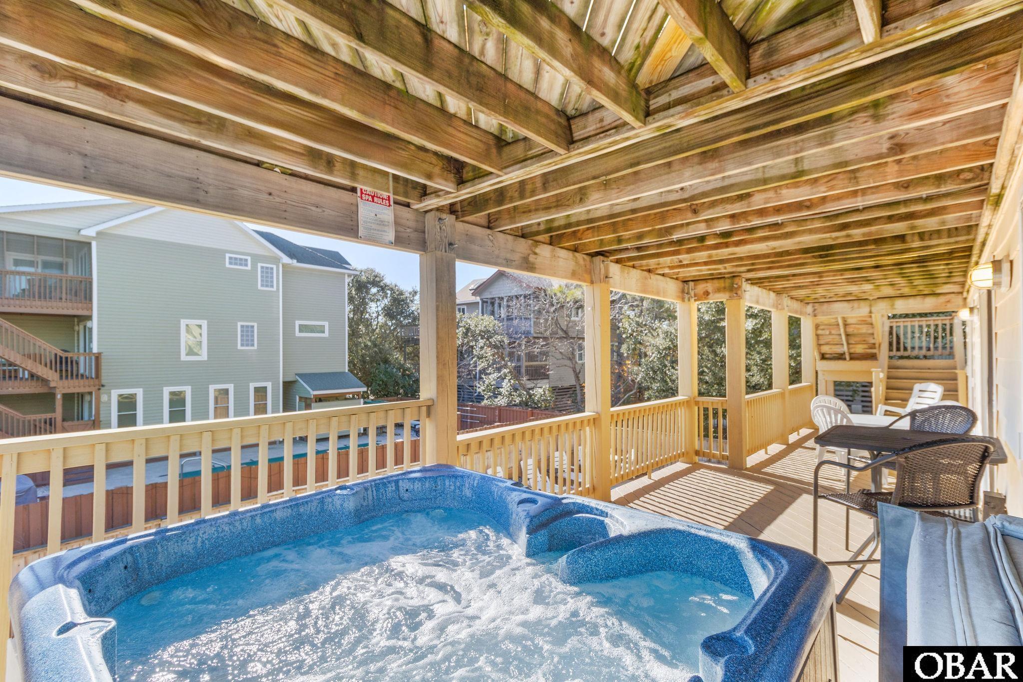 Bubbling hot tub on a covered wooden deck beside outdoor seating.