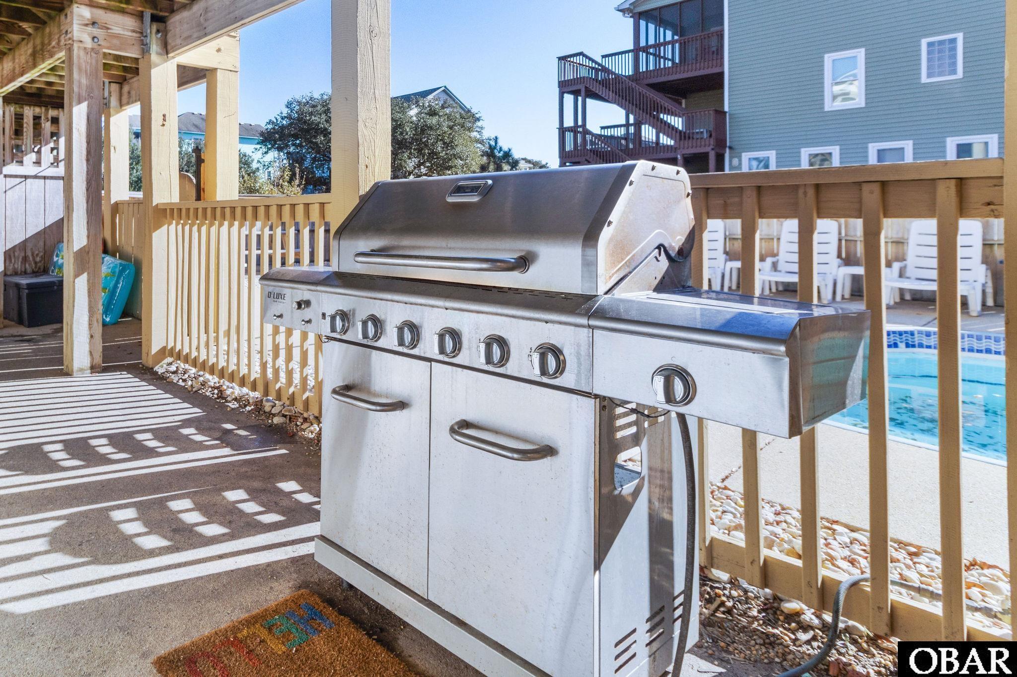 Outdoor deck with a stainless-steel grill beside a swimming pool.