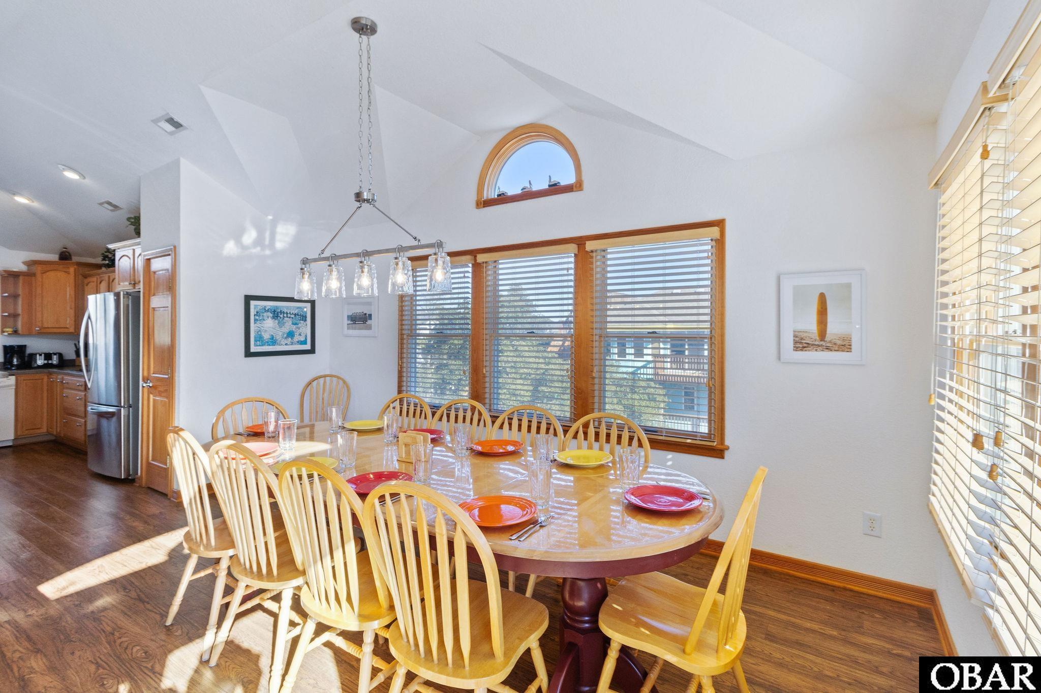 Dining room with a set oval table, spindle-back chairs, and large wood-trimmed windows.