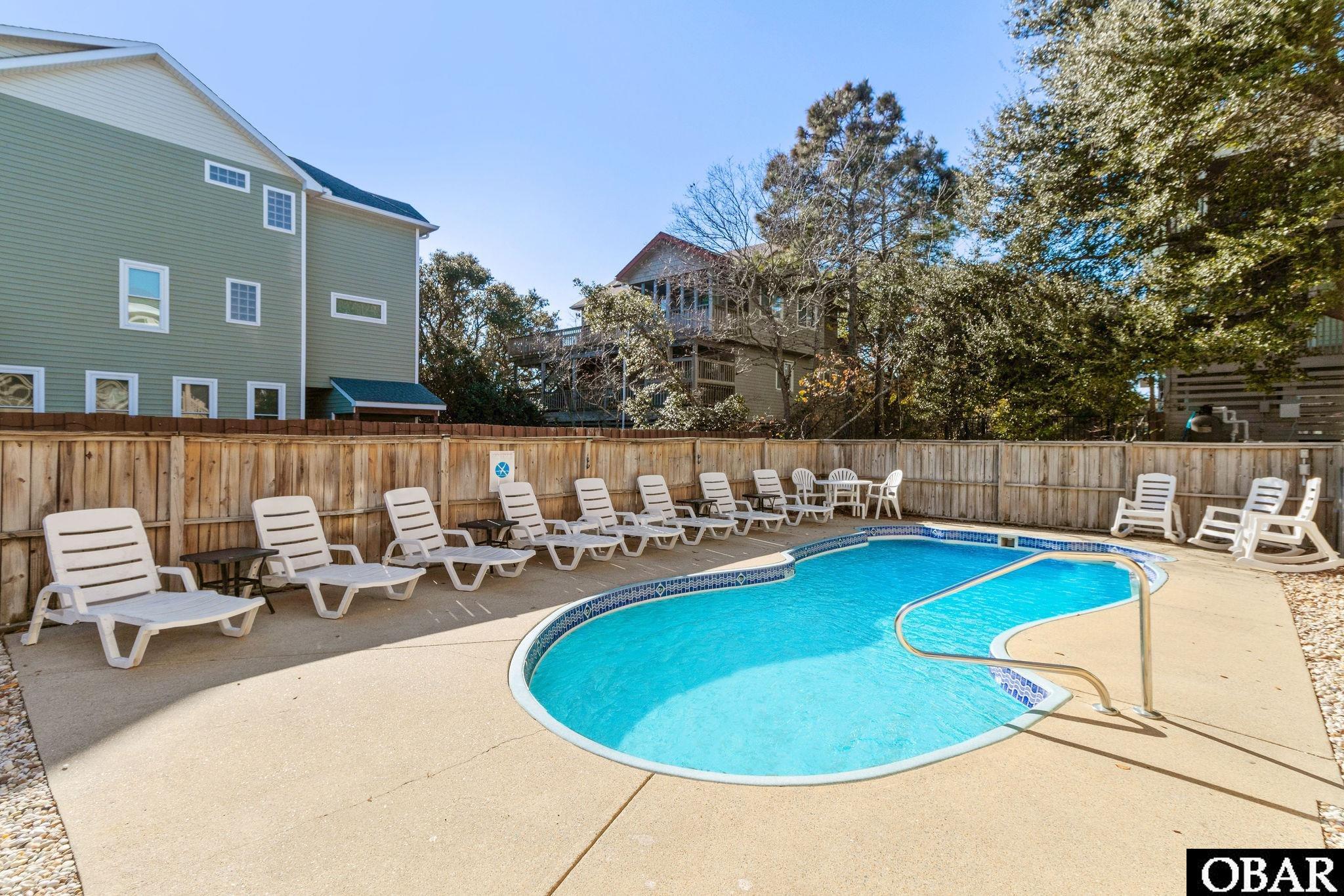 Outdoor swimming pool with a curved edge, metal handrail, and white lounge chairs.