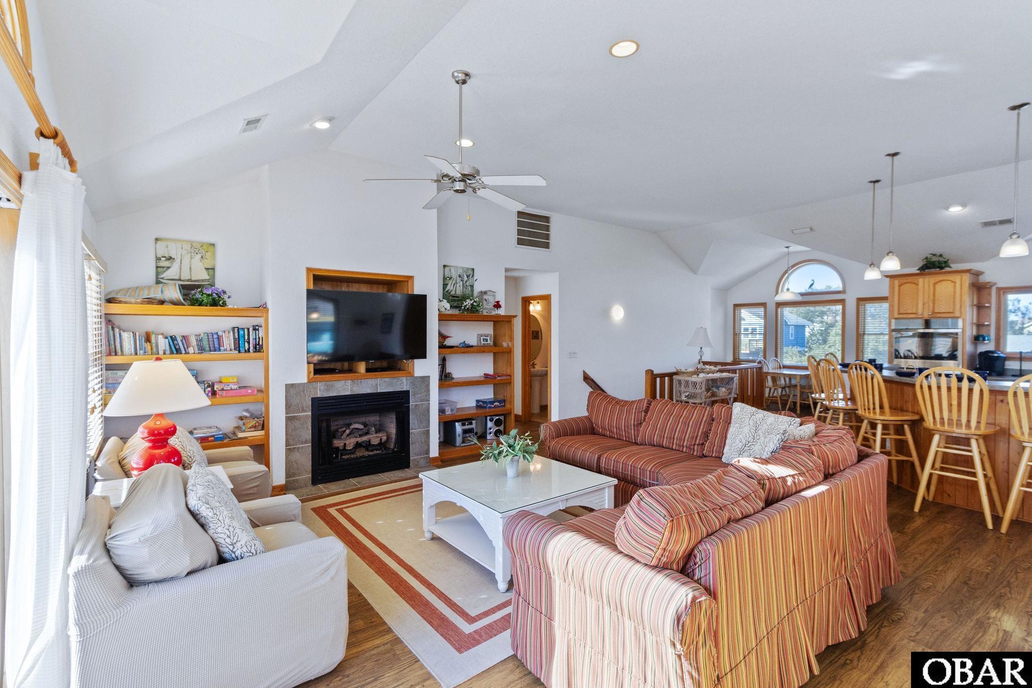 Open-plan living room with striped sofas, a fireplace, and built-in bookshelves beside the dining area.