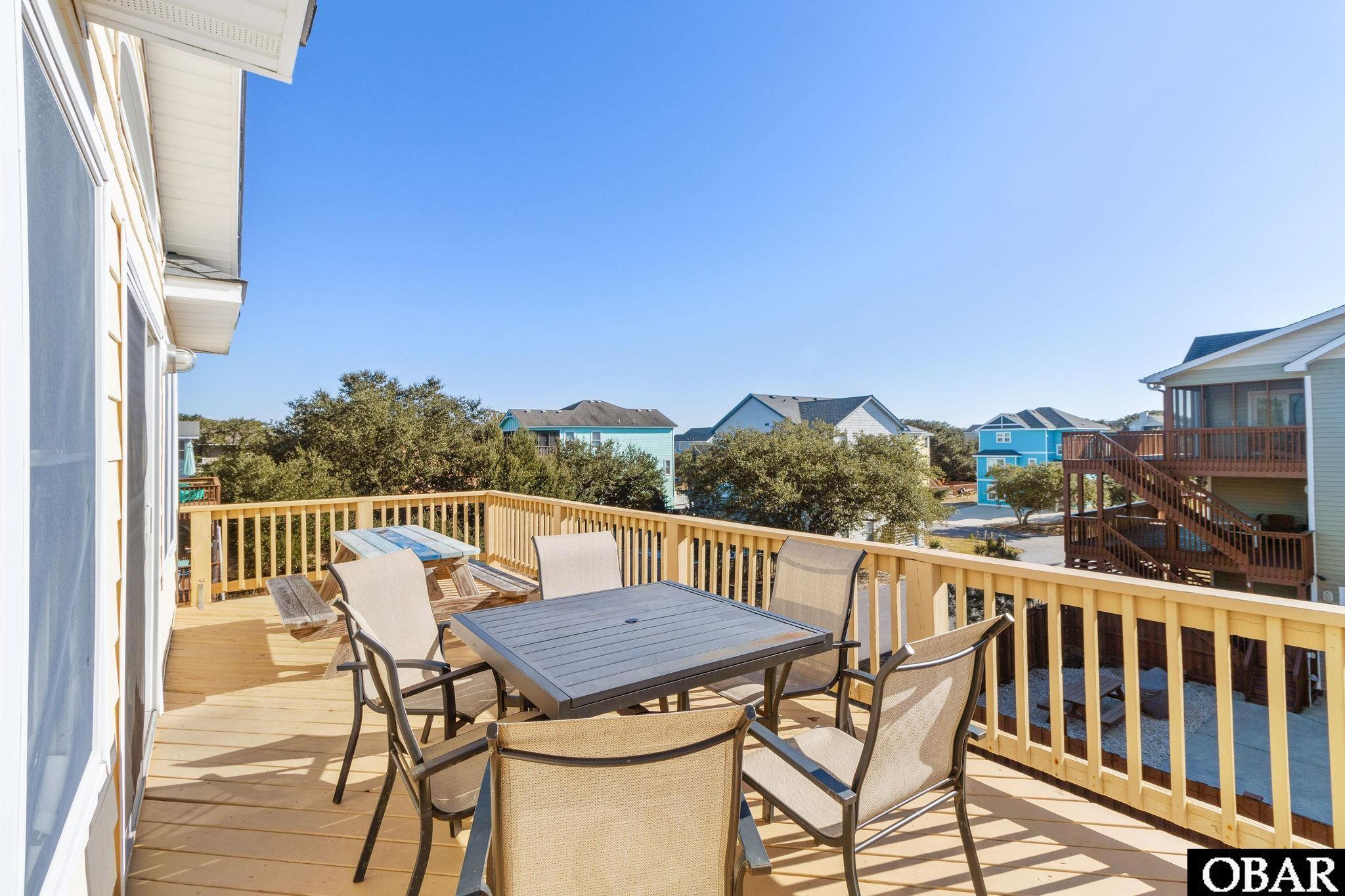 Furnished outdoor deck with a dining table and chairs overlooking nearby homes.