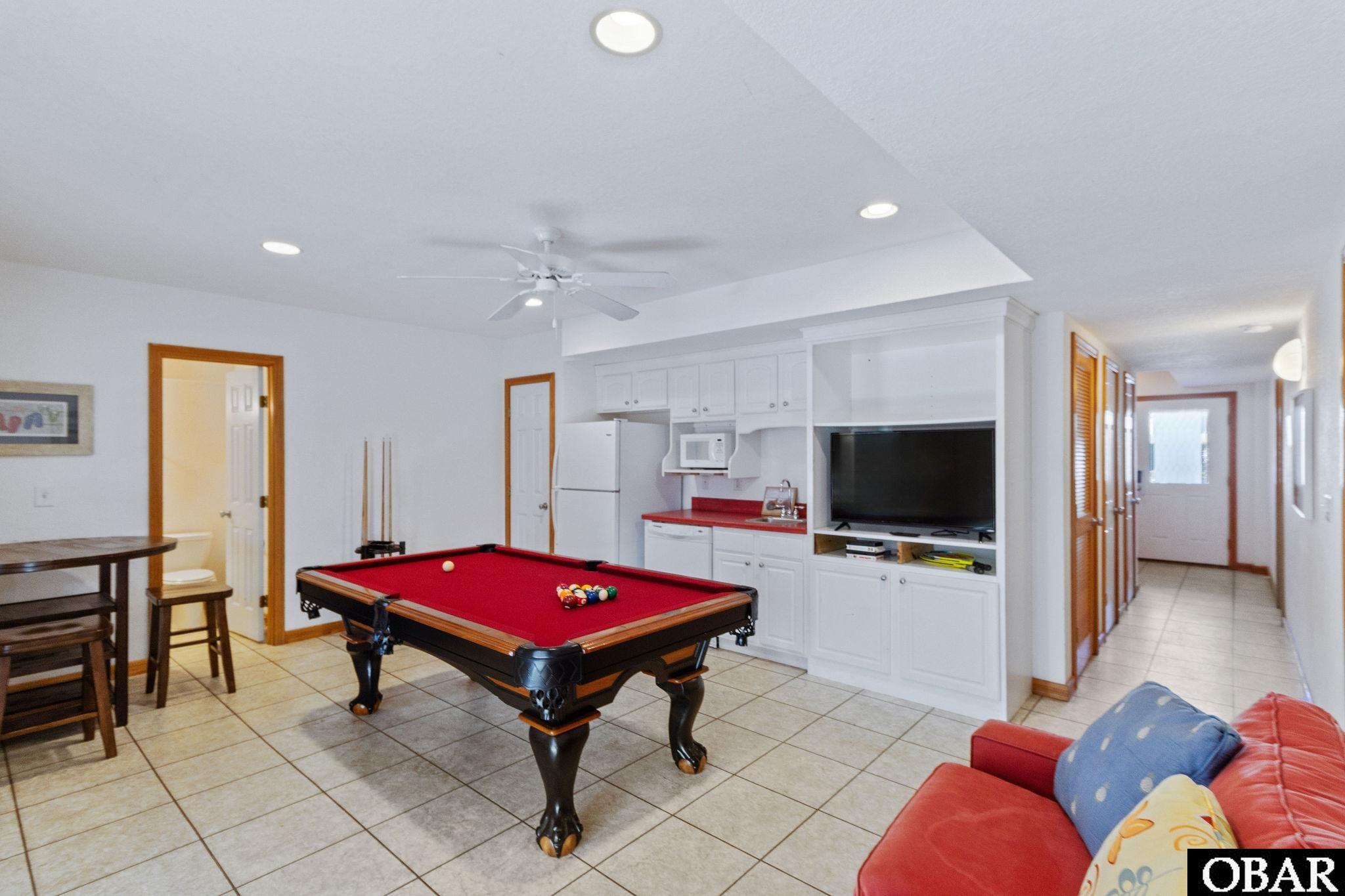 Game room with a red-felt pool table, built-in kitchenette and television, and red sofa.