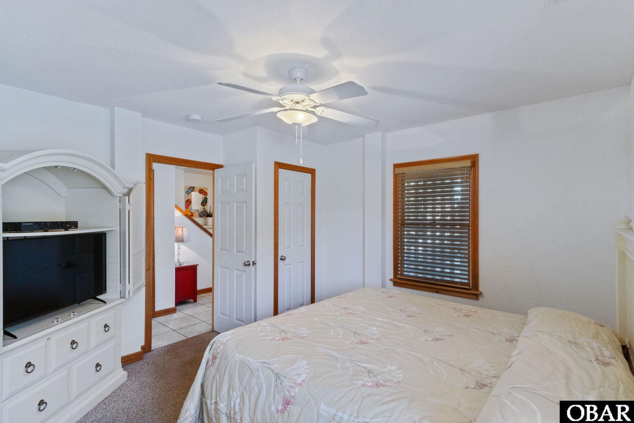 Bedroom with a floral bedspread, ceiling fan, and television in a built-in cabinet.