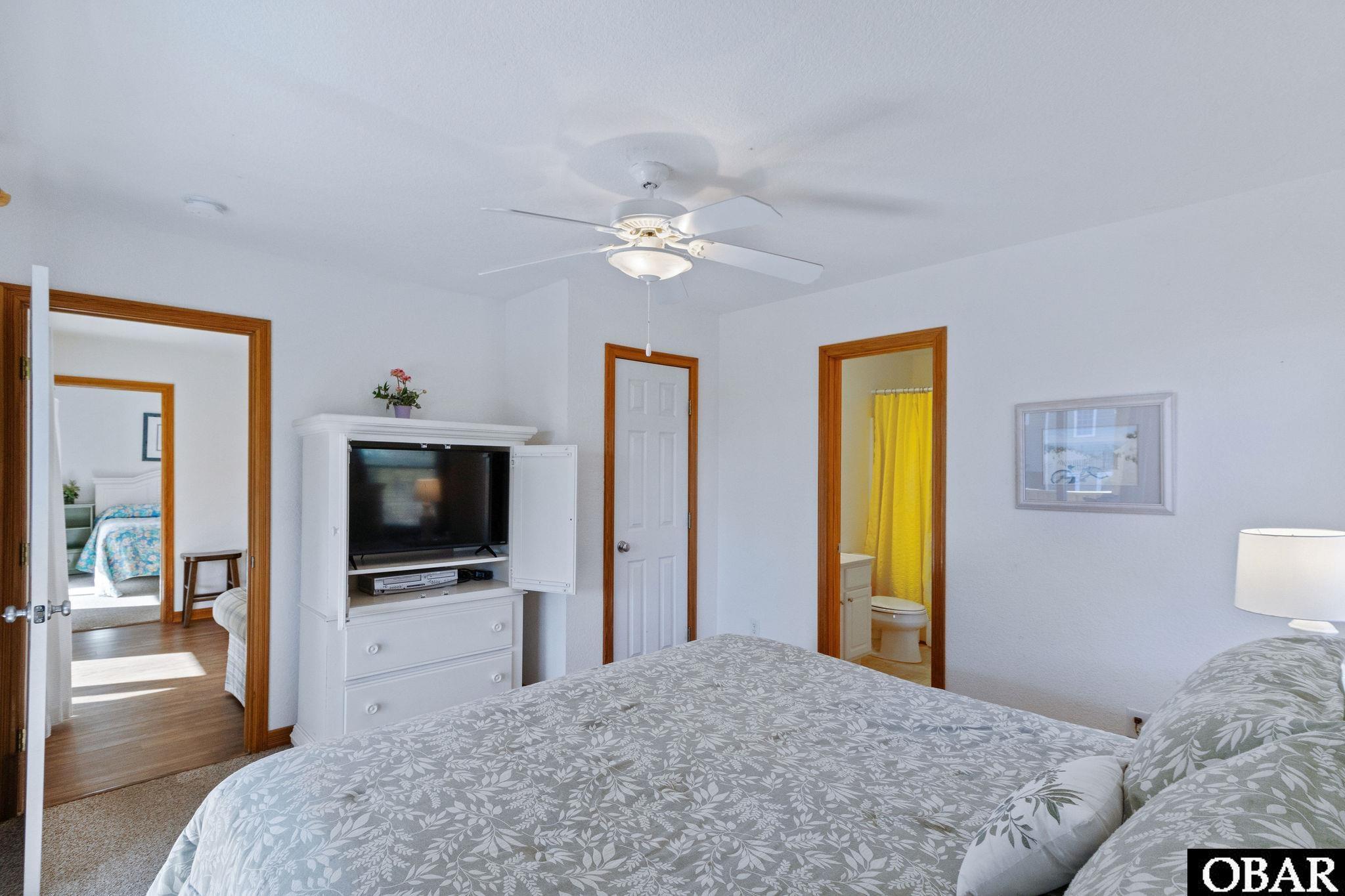 Bedroom with floral bedding, a television dresser, and a bathroom doorway with a yellow shower curtain.