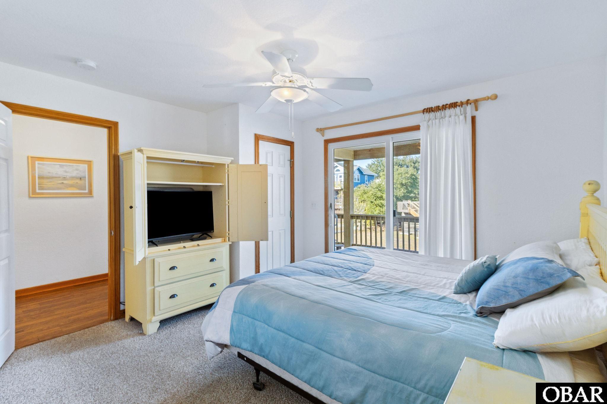 Furnished bedroom with blue bedding, a TV armoire, and sliding doors to a deck.
