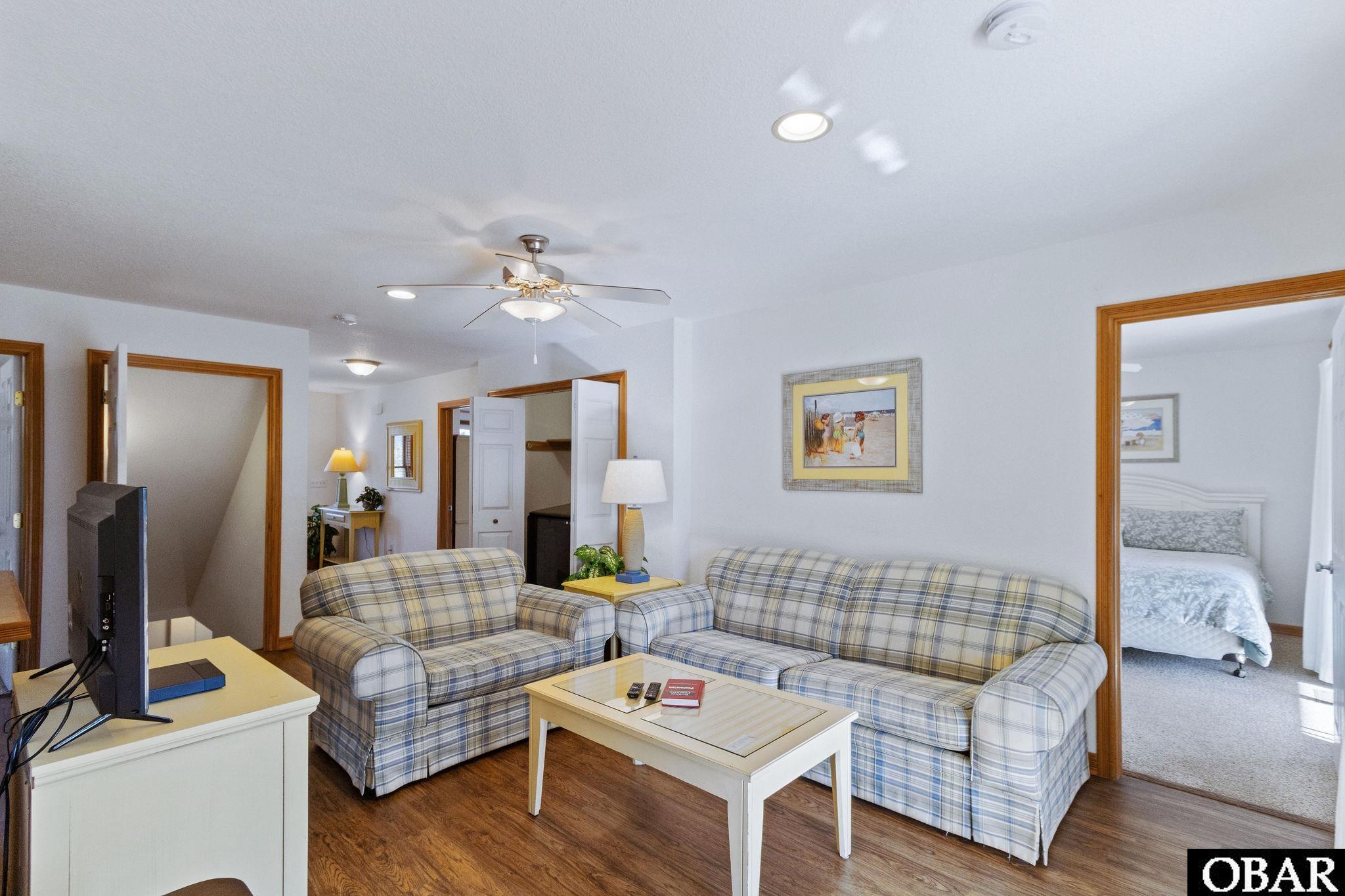 Living room with plaid sofas and a white coffee table, viewed toward an open bedroom doorway.