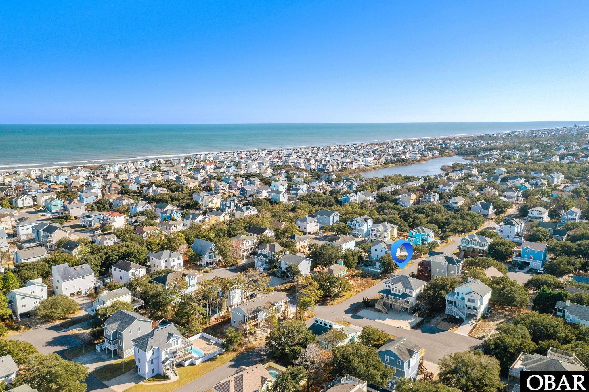 Aerial view of a coastal neighborhood, with the ocean, inland pond, and blue location marker.