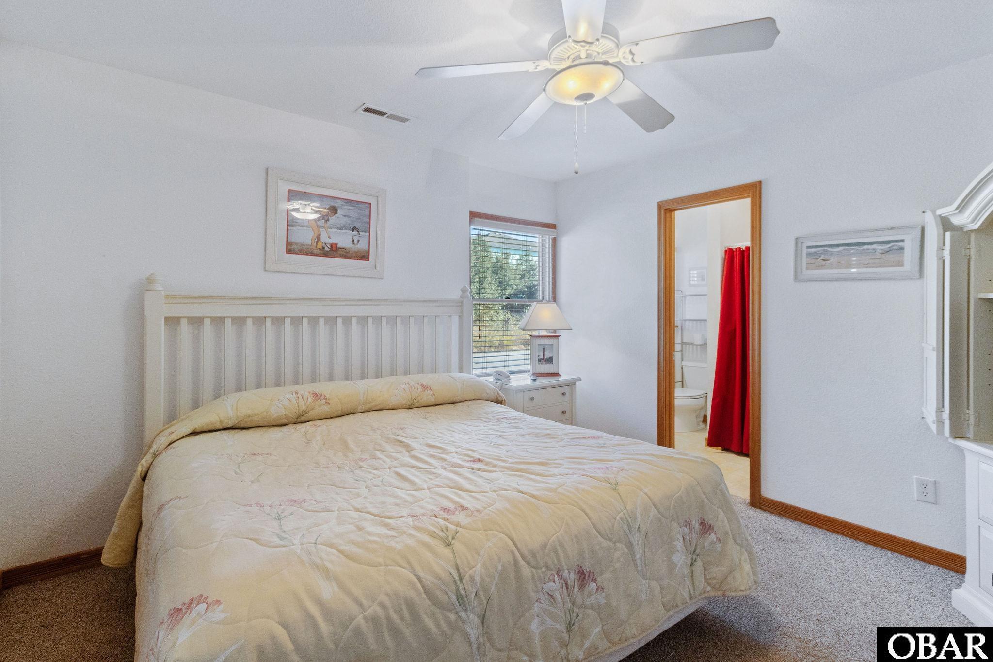 Bedroom with a floral quilted bed, ceiling fan, and bathroom doorway with a red shower curtain.