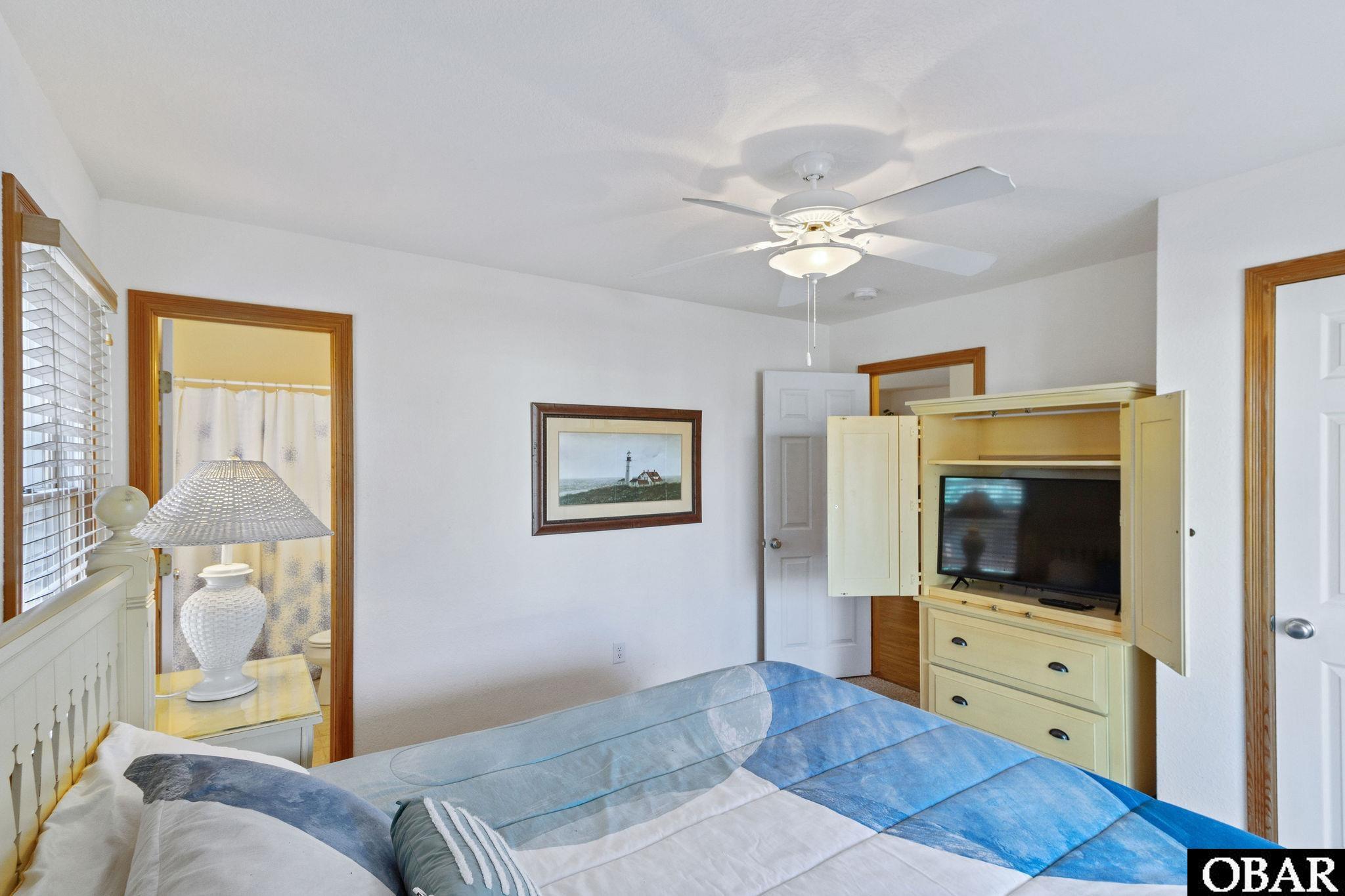 Bedroom with blue-and-white bedding, a ceiling fan, and a television in a pale yellow cabinet.