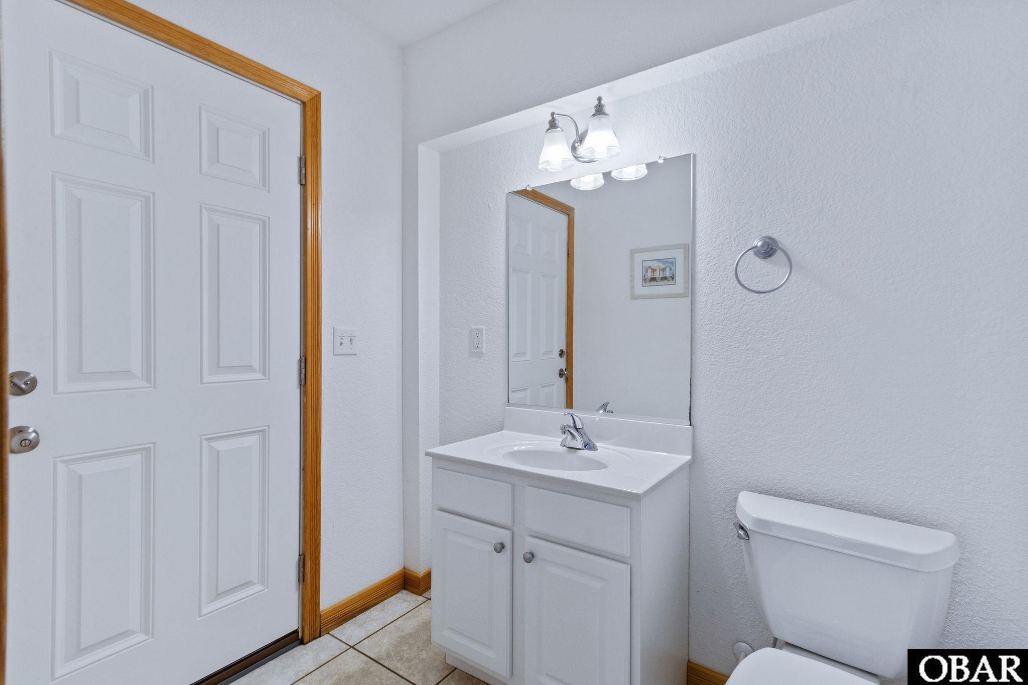 Bathroom with a white vanity and large mirror beside a toilet and white door.
