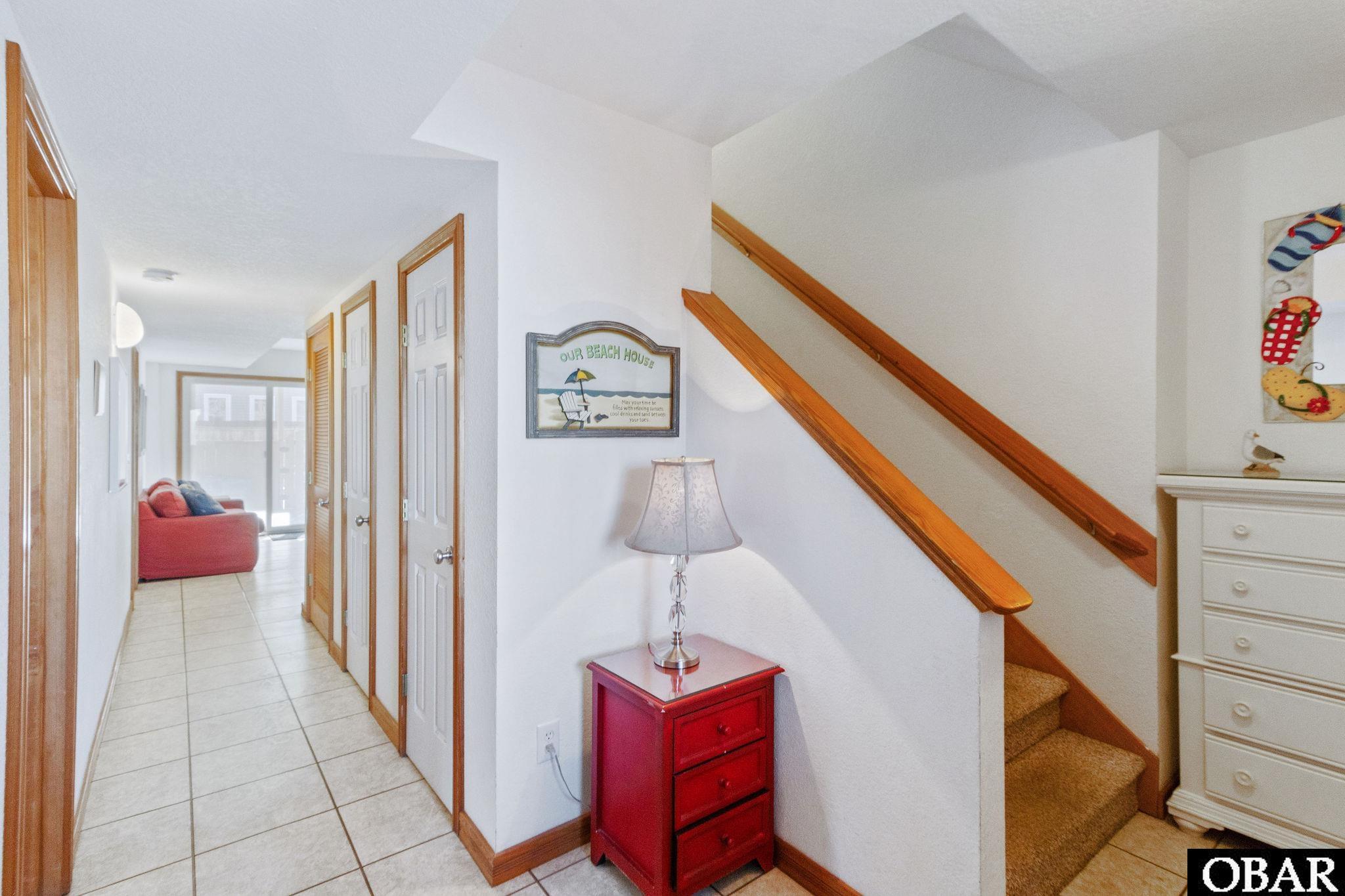 Tiled hallway beside a carpeted staircase with wood railings, a red chest, and a glimpse of a red sofa.