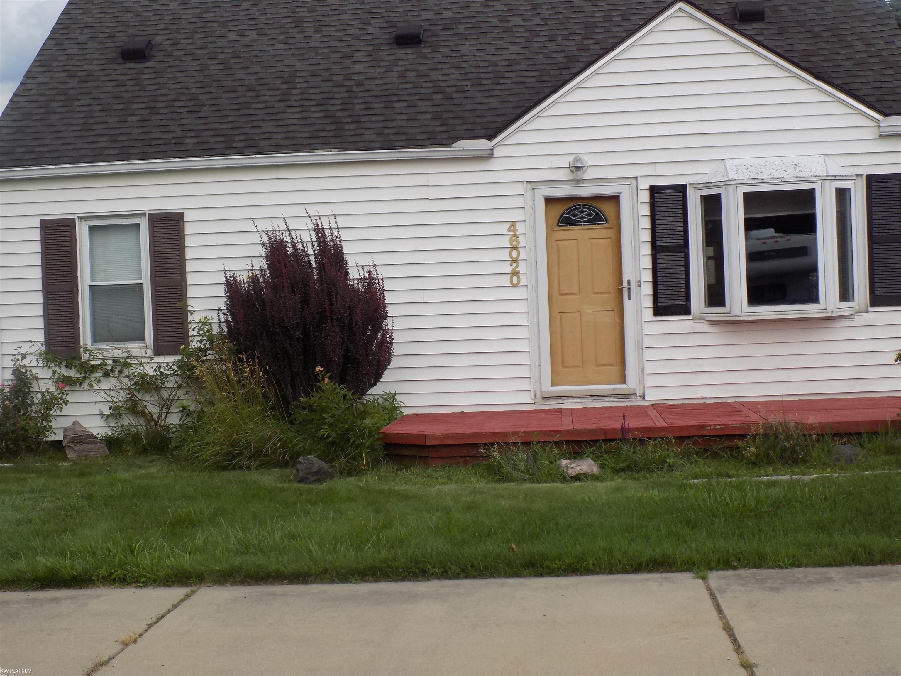 House front with white siding, tan entry door, bay window, and red porch deck.