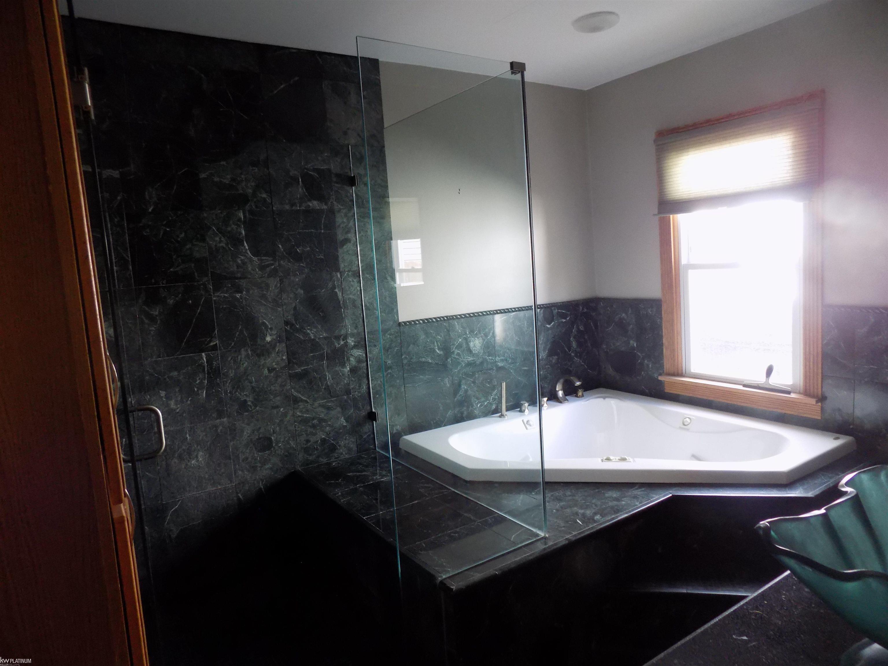 Bathroom with a white corner jetted tub, glass shower enclosure, and dark marble tile.