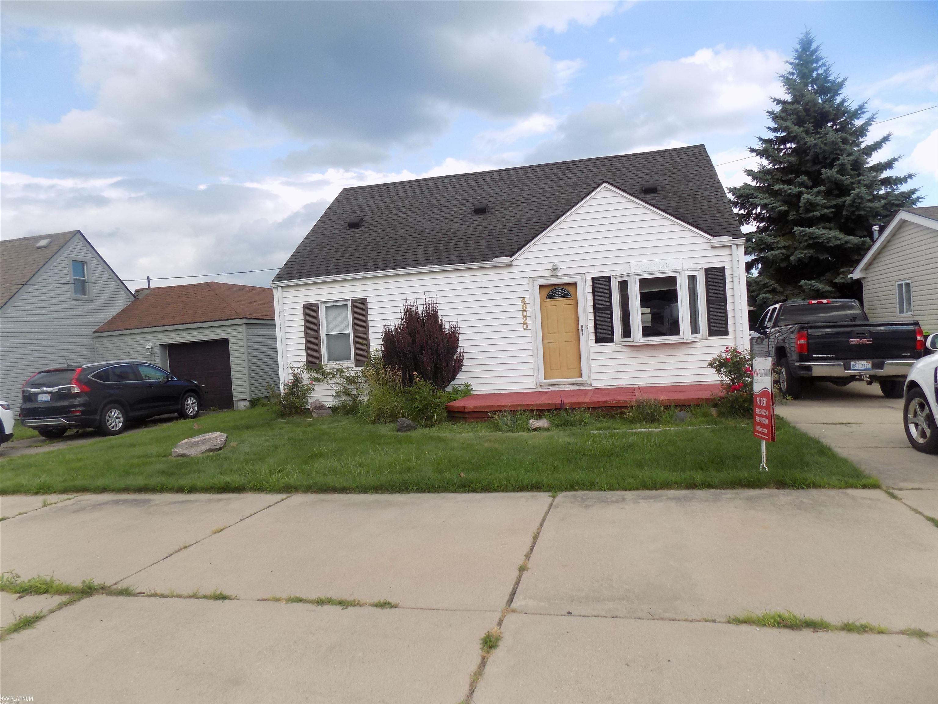 White-sided house with a steep dark roof, tan front door, and red-painted front deck.