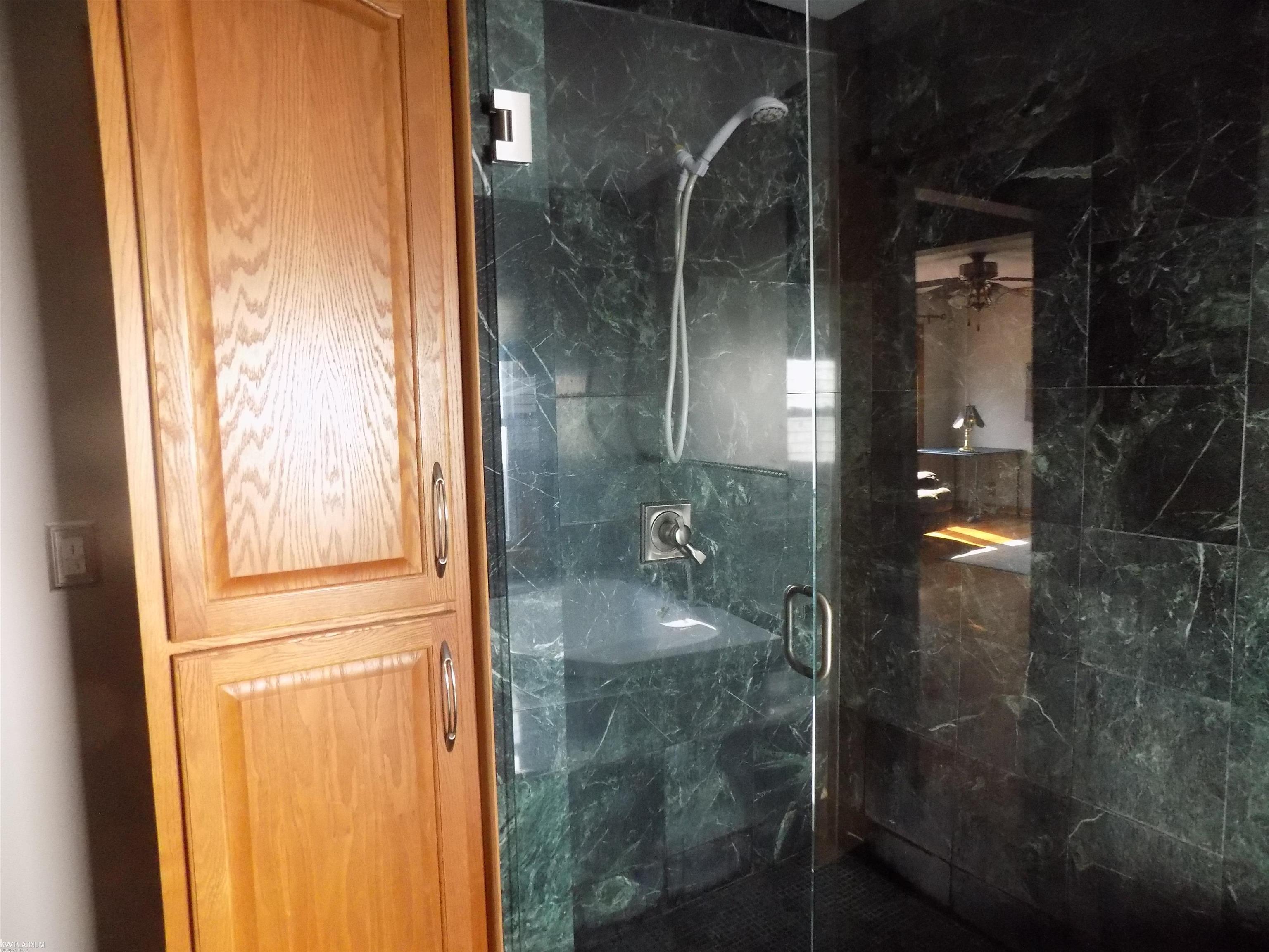Bathroom shower with dark green marble-look tile, glass enclosure, and a warm oak cabinet.