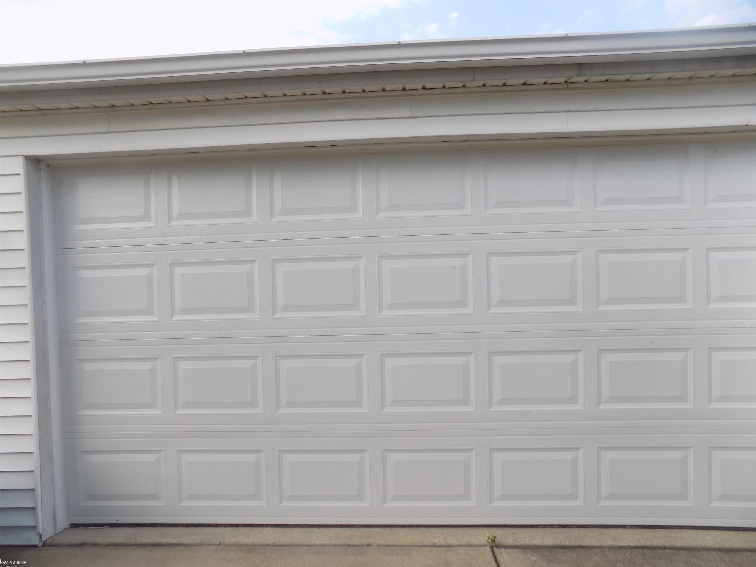 White paneled garage door beneath a broad roof eave, with siding and concrete driveway.