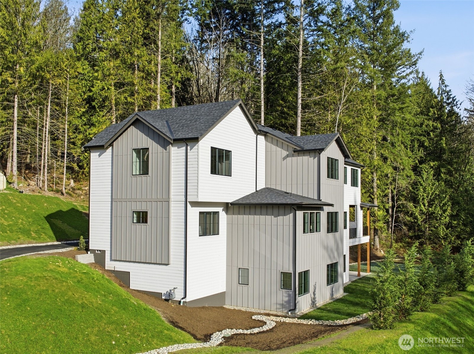 Modern two-story white and taupe house on a wooded, sloping lot.