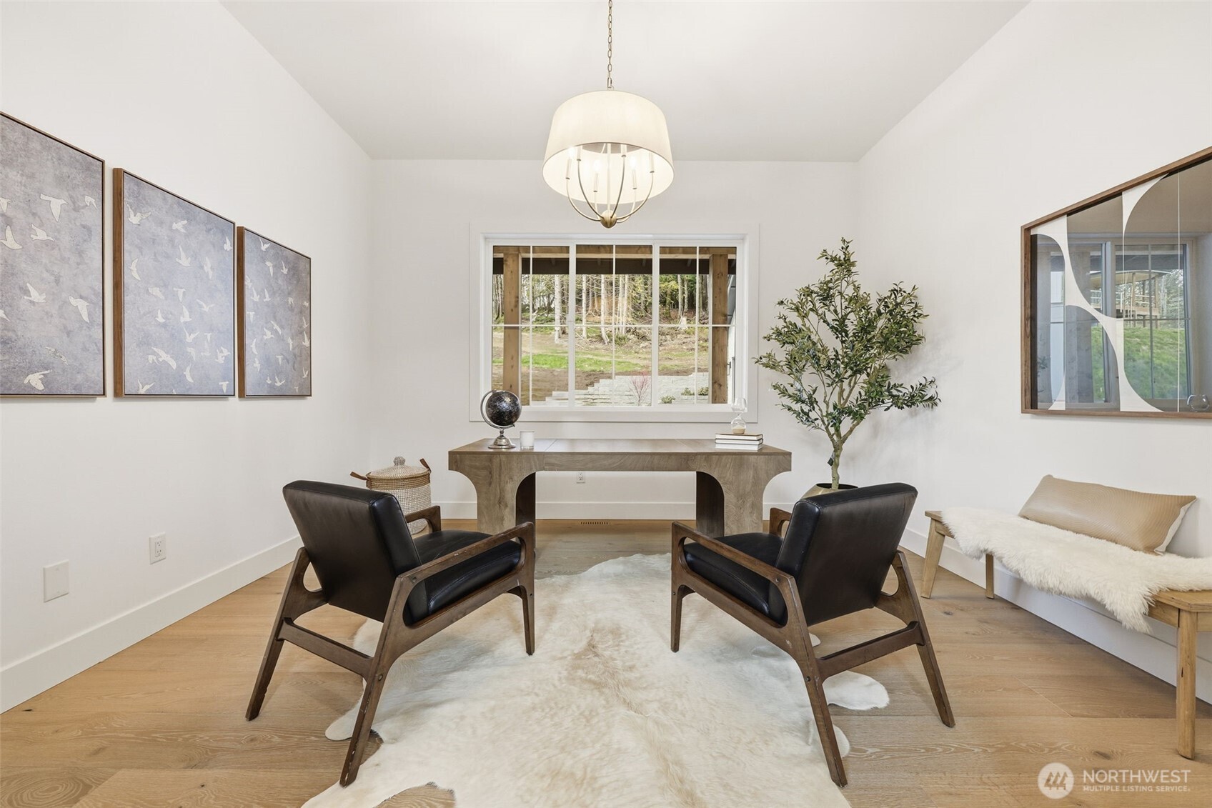 Staged home office with a wooden desk, two leather chairs, and a large window overlooking greenery.
