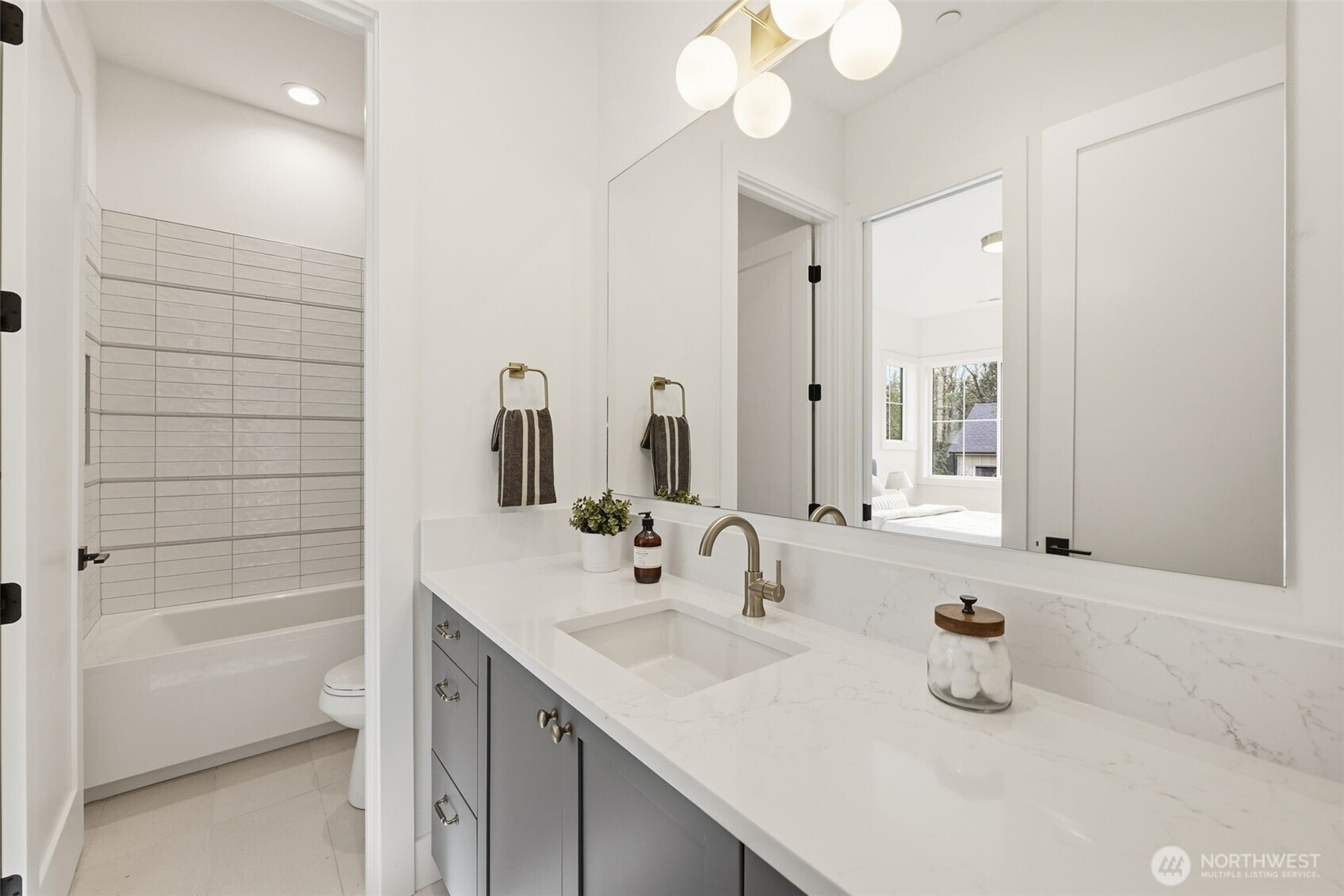 Modern bathroom with a long white vanity and a gray-tiled tub-and-shower alcove.